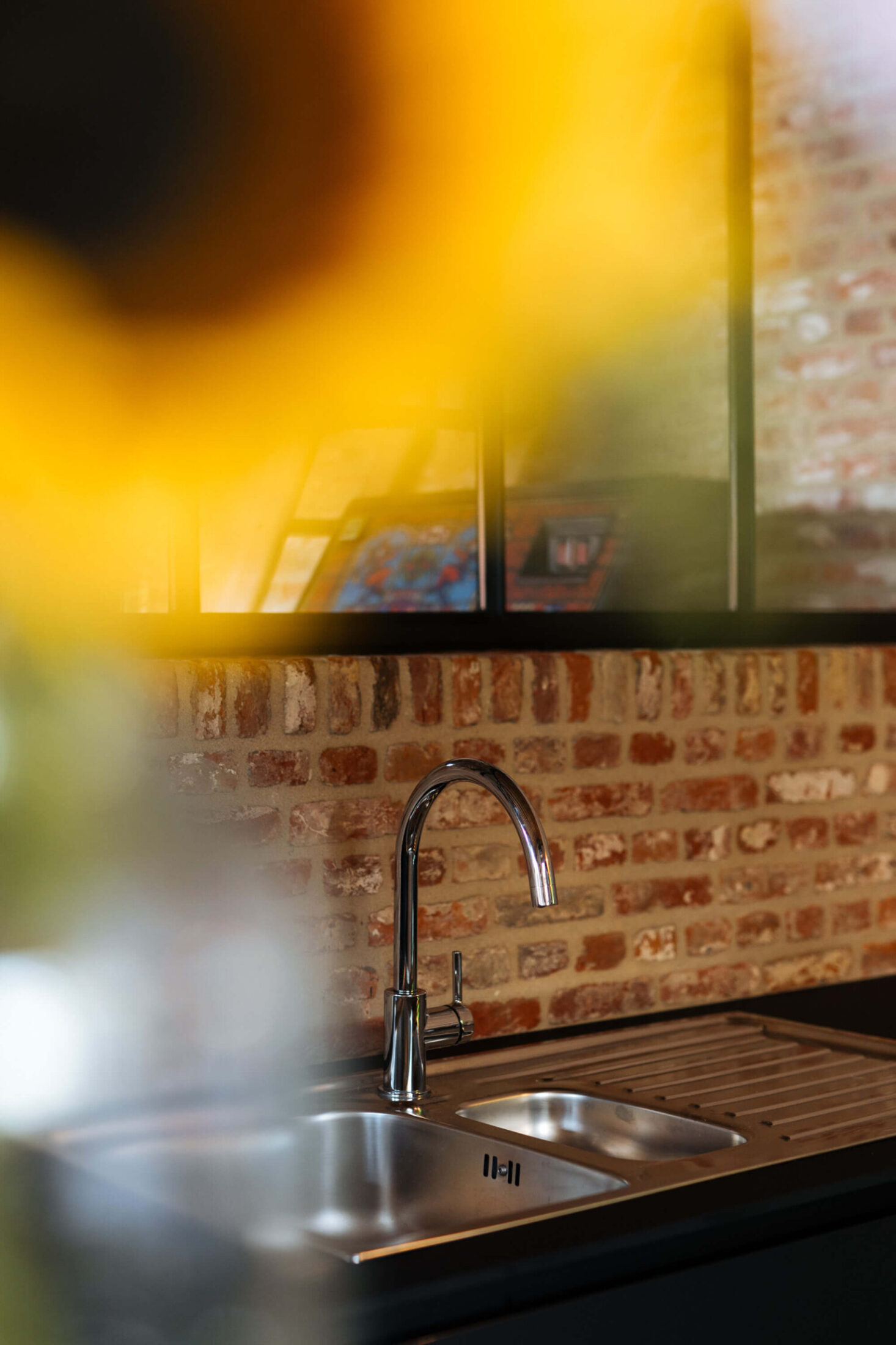 Detail van een bar op maat met inox spoelbak en kraan voor een bakstenen muur in Beveren, Kaster Keukens