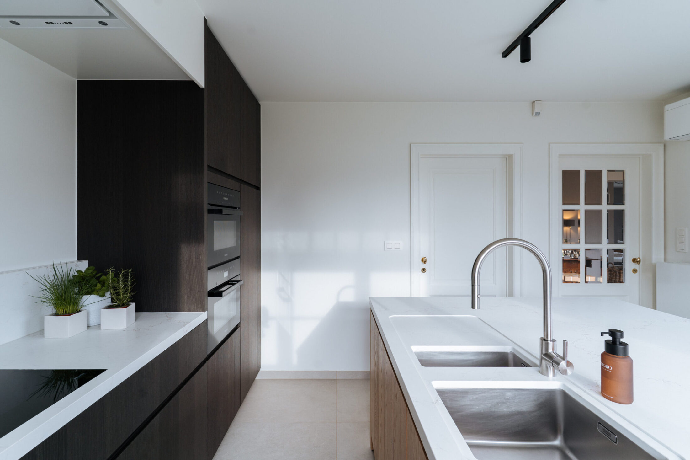Moderne keuken met donkere houten fronten, wit werkblad en dubbele inox spoelbak in Berlare, Kaster Keukens