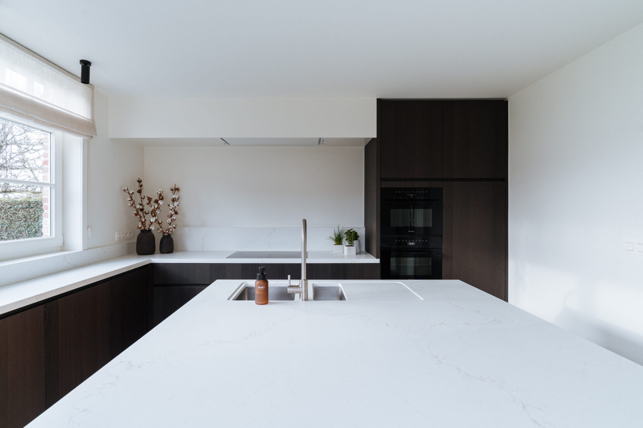 Moderne keuken met wit kookeiland, donkere houten kasten en raam in Berlare, Kaster Keukens