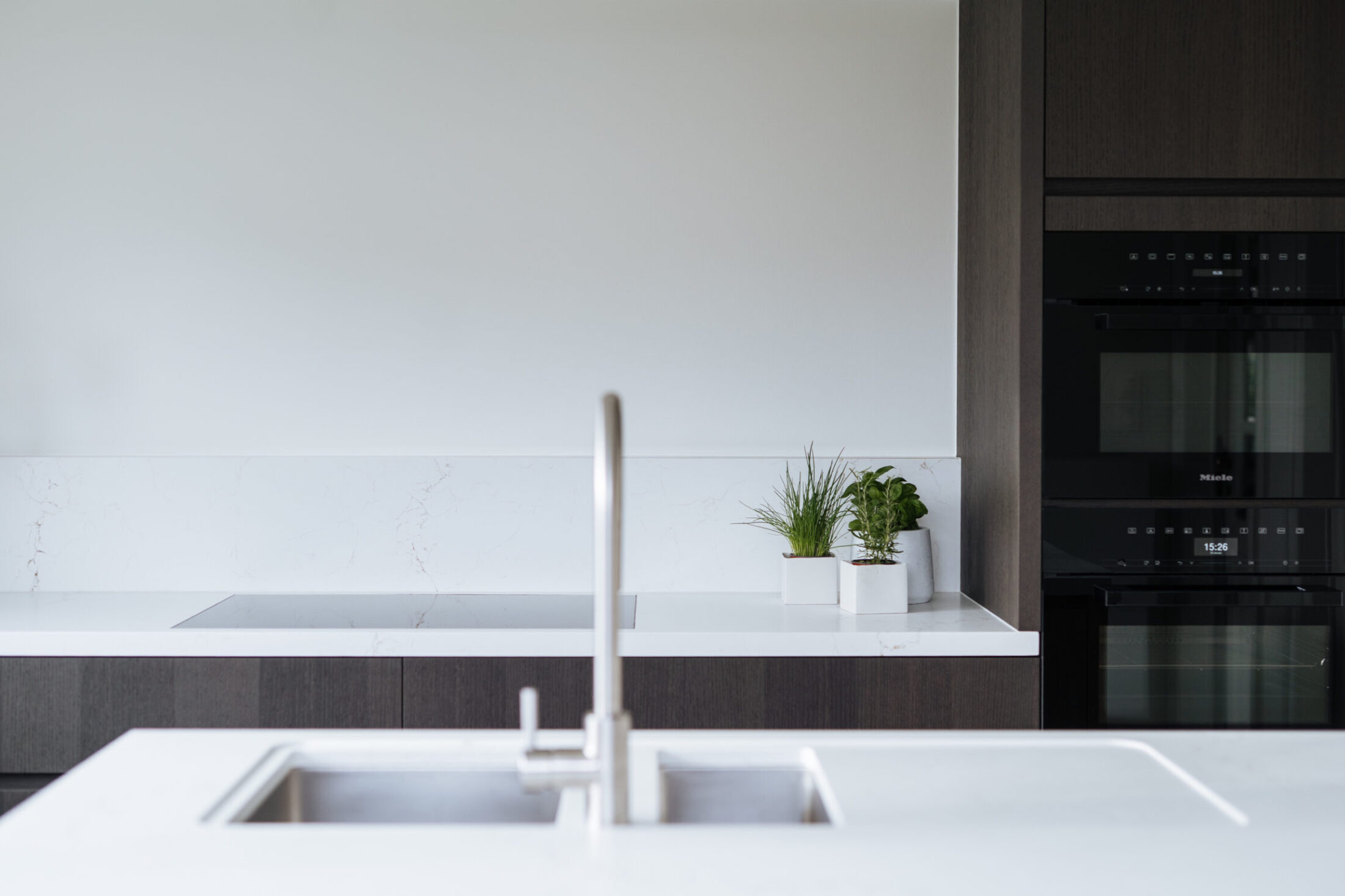 Detail van een moderne keuken met inox spoelbak in wit werkblad en donkere ovenkast in Berlare, Kaster Keukens