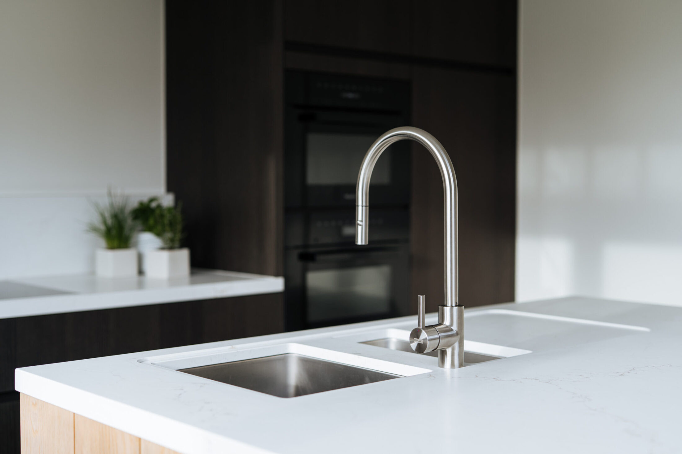 Detail van een moderne keuken met inox kraan, dubbele spoelbak en eiken zijkant in Berlare, Kaster Keukens