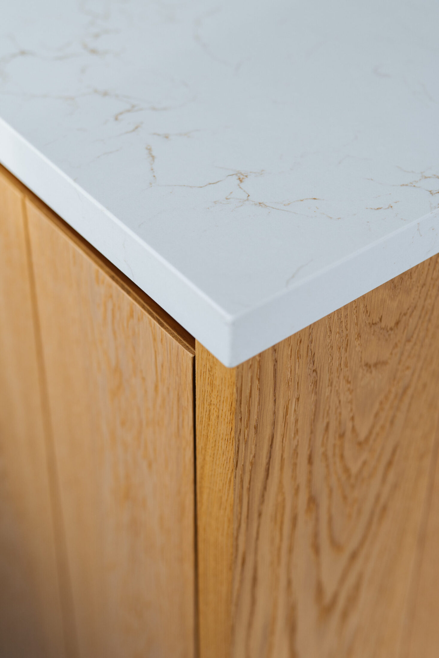 Detail van een moderne keuken met wit werkblad met lichte adering op een eiken zijpaneel in Berlare, Kaster Keukens