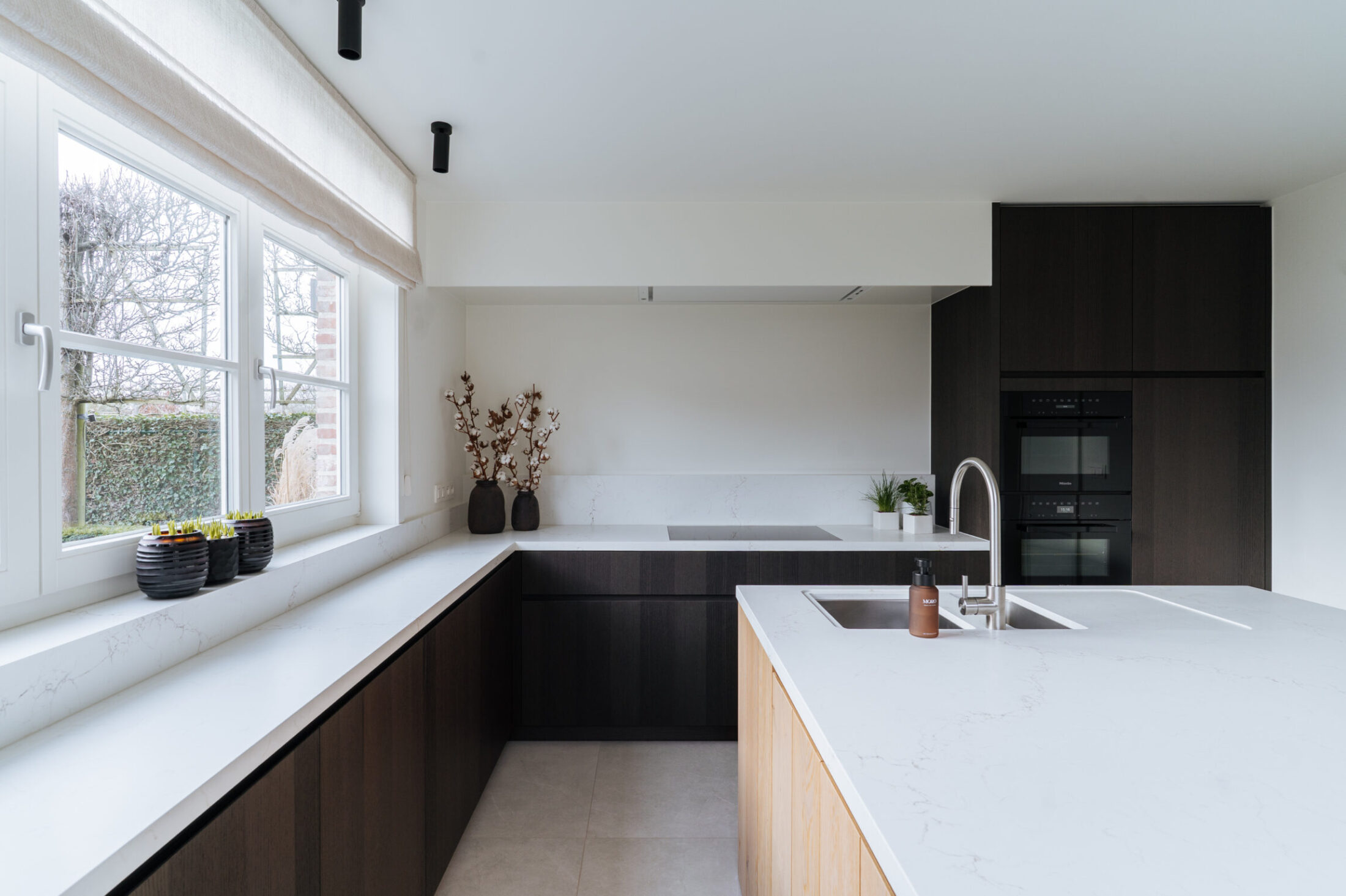 Moderne keuken in U-vorm met donkere houten fronten, wit werkblad en eiland met eiken zijkant in Berlare, Kaster Keukens