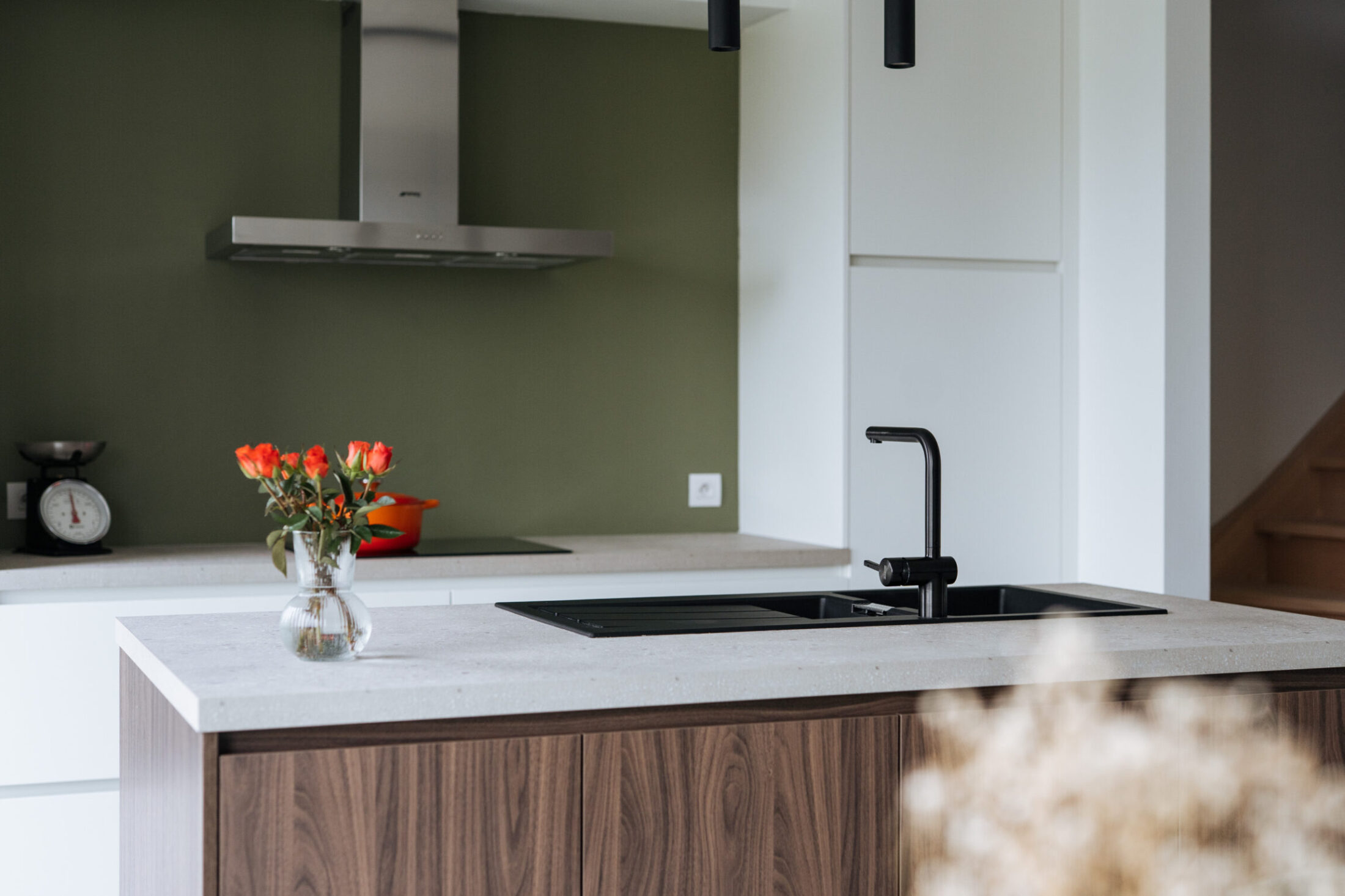 Moderne keuken met notelaar eiland, licht werkblad, zwarte kraan en groene achterwand in Meulebeke, Kaster Keukens