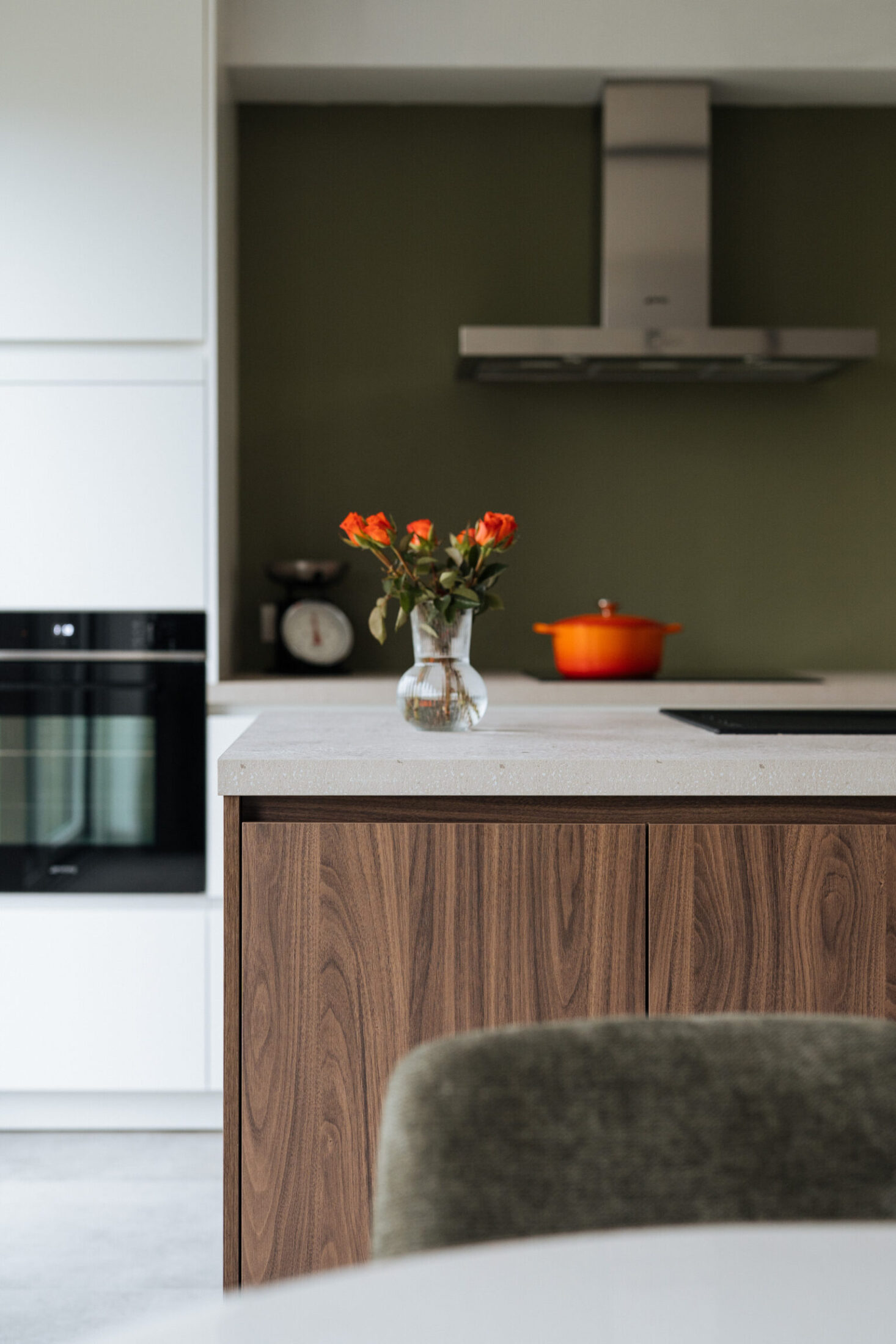 Detail van een moderne keuken met groene achterwand, inox dampkap en witte hoge kast met oven in Meulebeke, Kaster Keukens