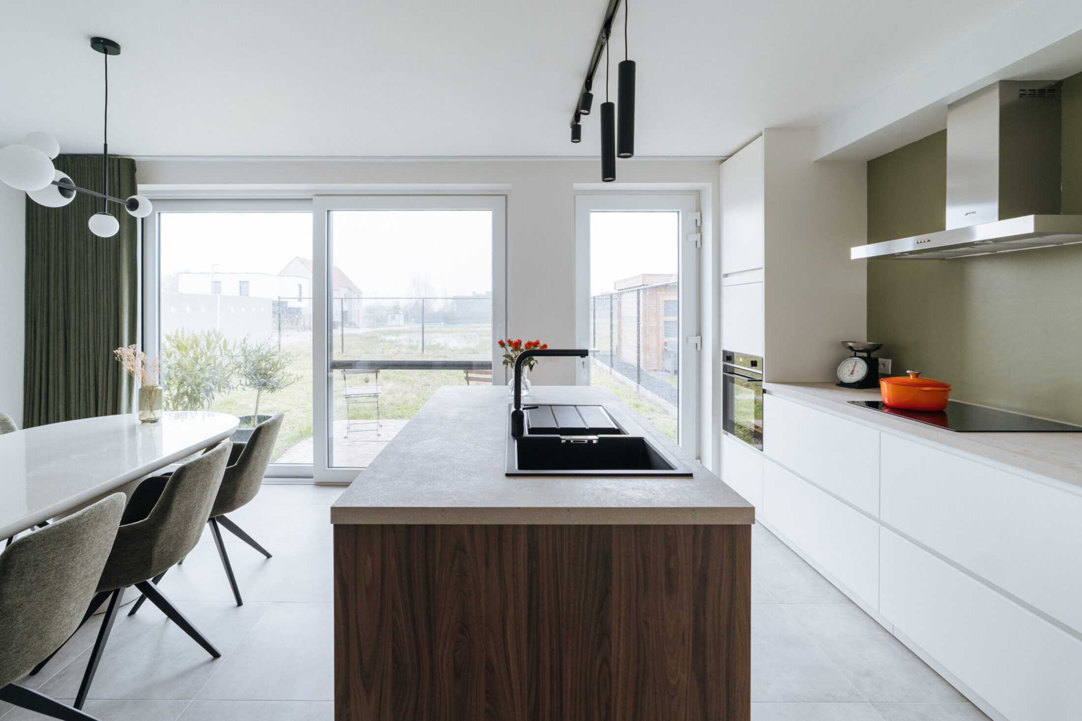 Moderne keuken met notelaar kookeiland, witte fronten en eettafel bij de raampartij in Meulebeke, Kaster Keukens