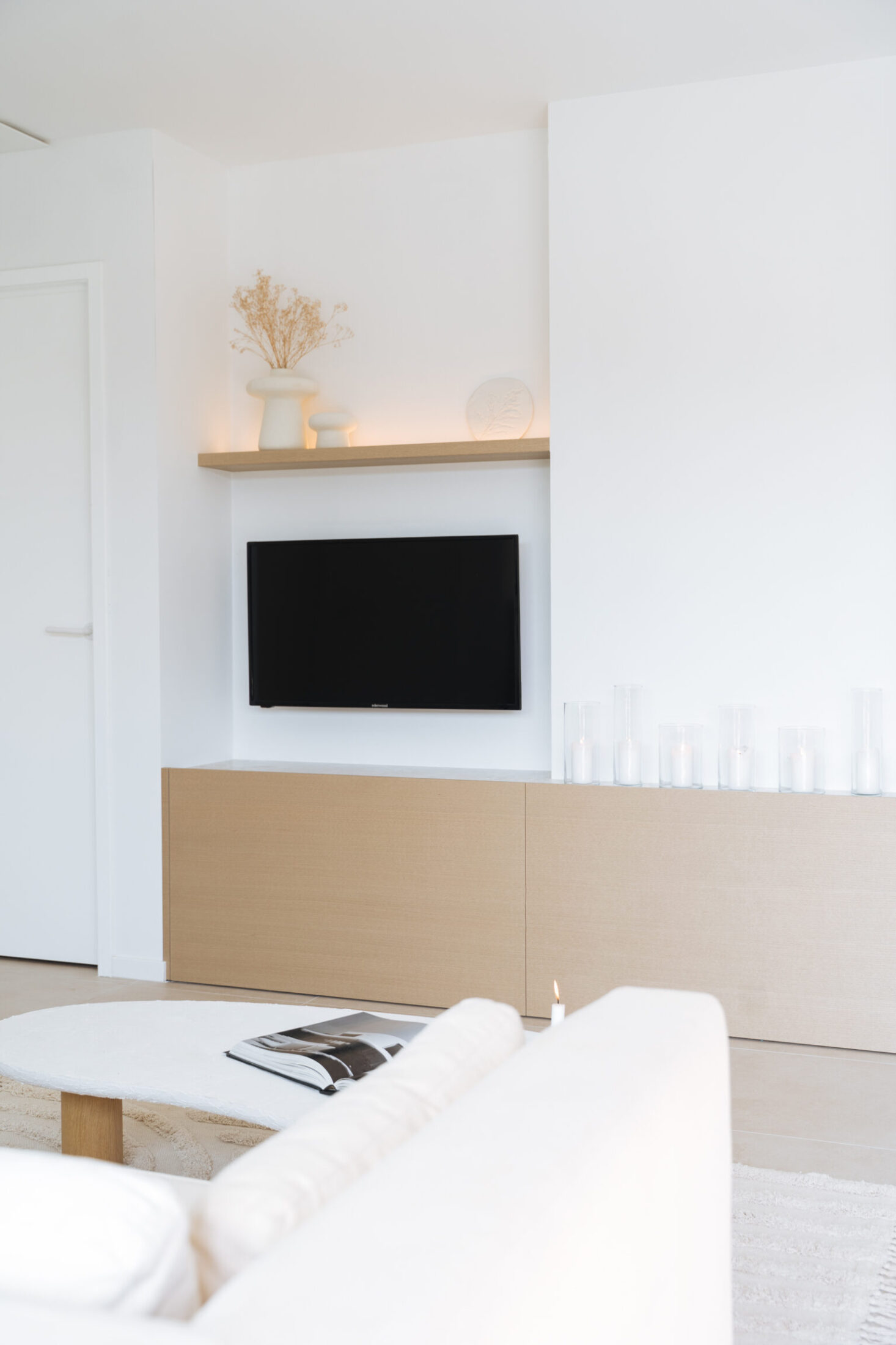 Tv-meubel op maat met eiken onderkast en verlichte wandplank in de leefruimte in Middelkerke, Kaster Keukens