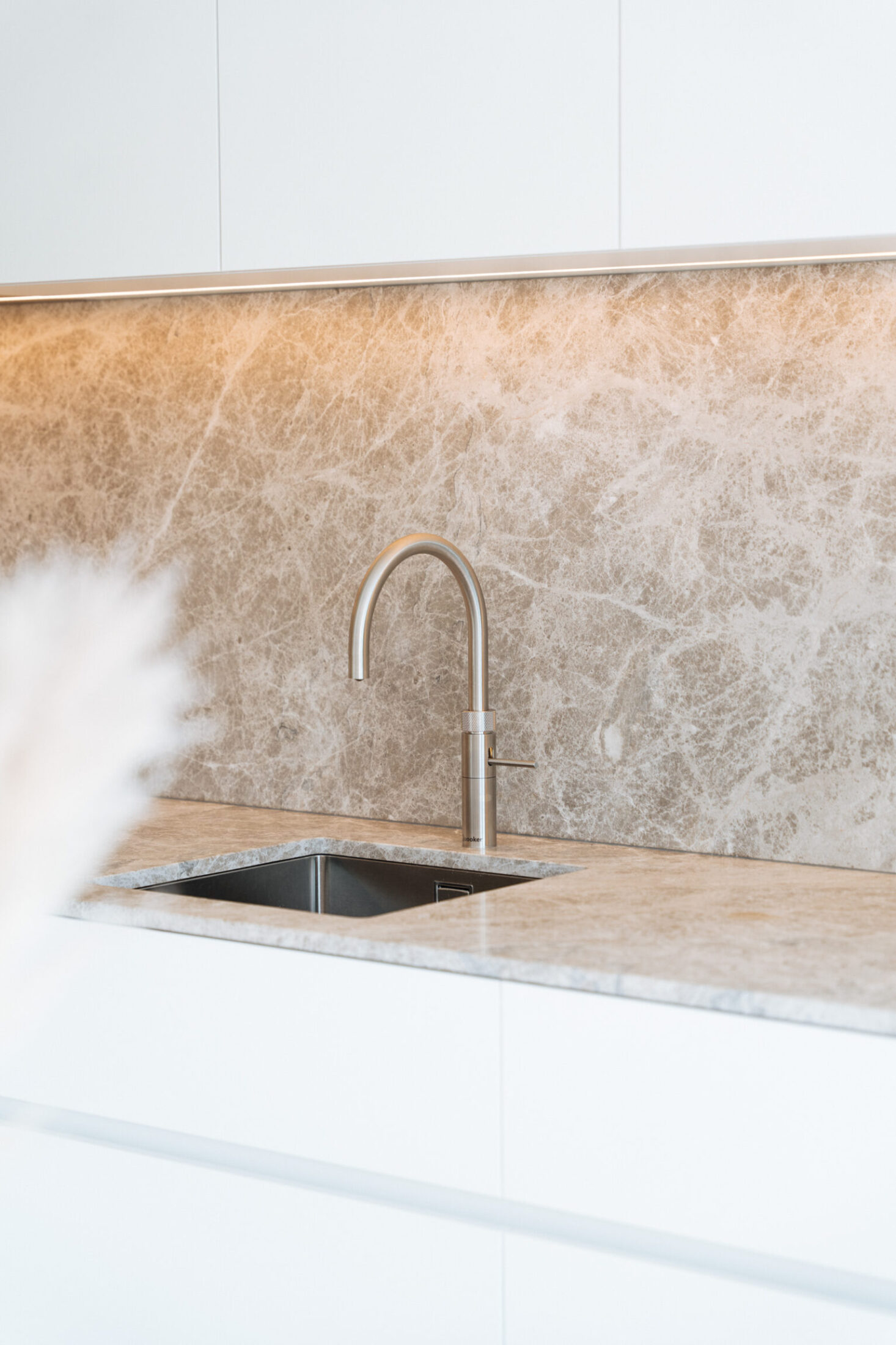 Detail van een moderne keuken met beige marmerlook achterwand, inox spoelbak en kraan in Middelkerke, Kaster Keukens