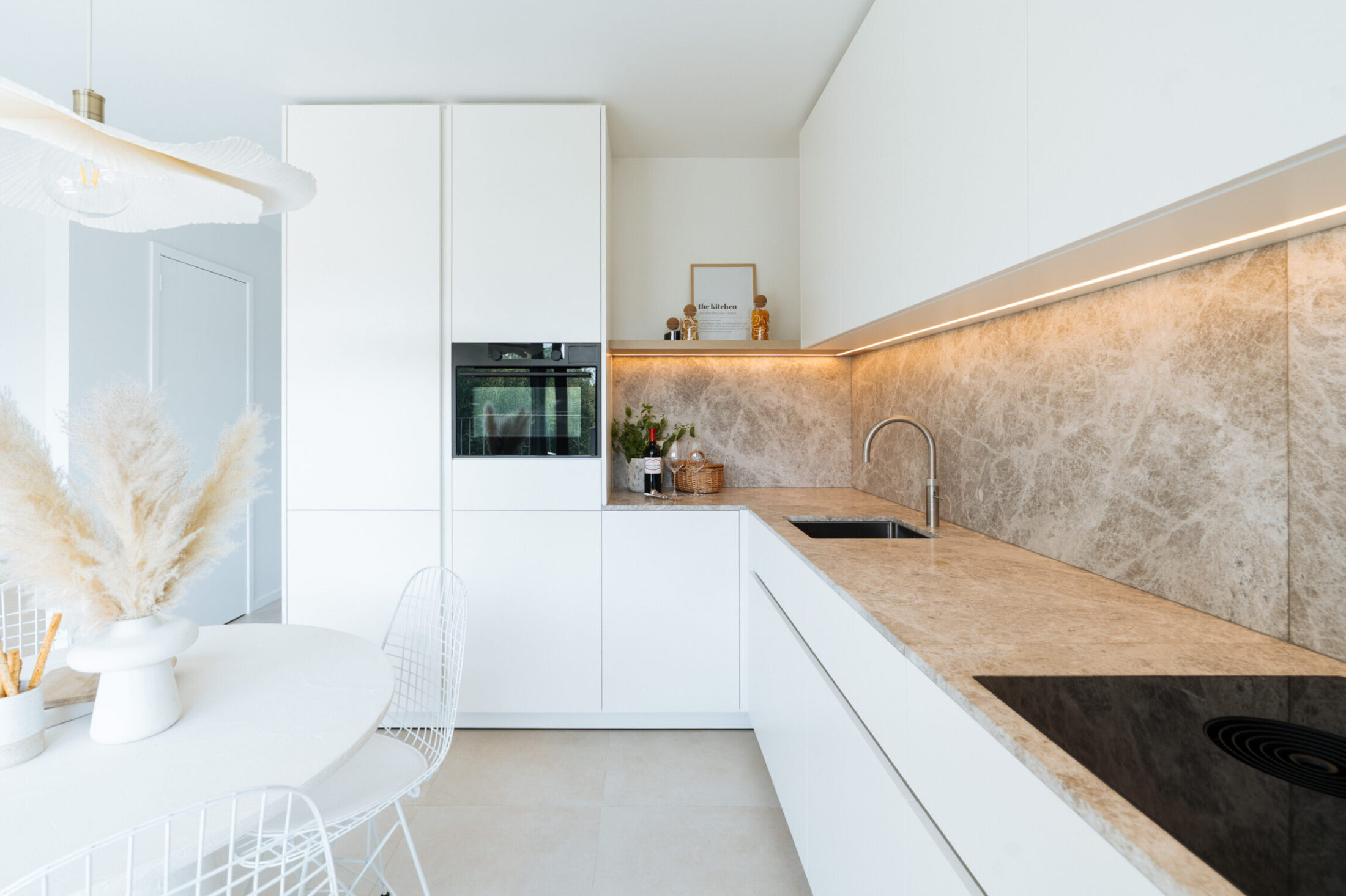 Moderne keuken met witte fronten, beige marmerlook werkblad, ledverlichting en kookplaat in Middelkerke, Kaster Keukens