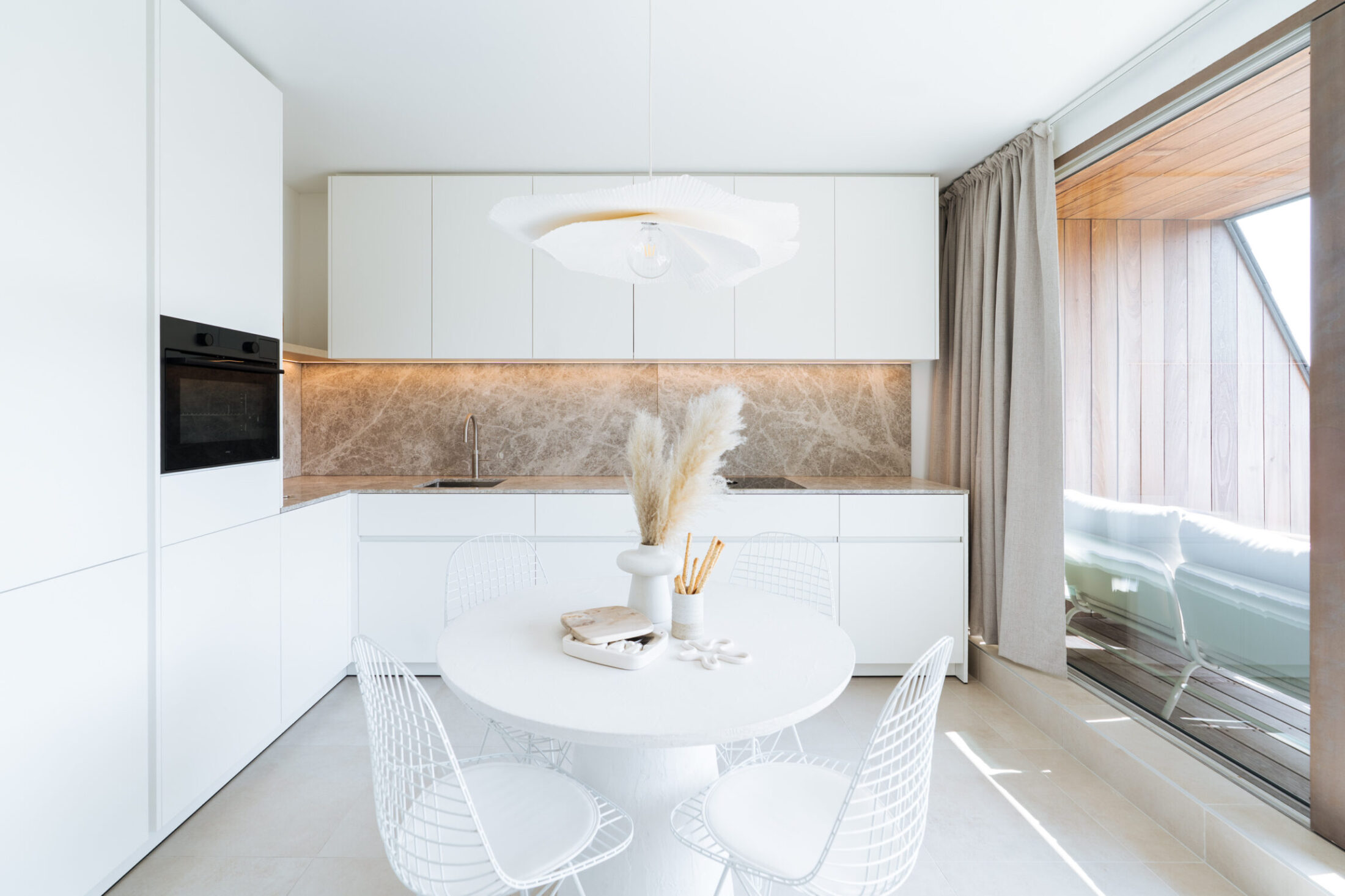 Moderne keuken met witte kasten, ronde eettafel en grote raampartij in Middelkerke, Kaster Keukens