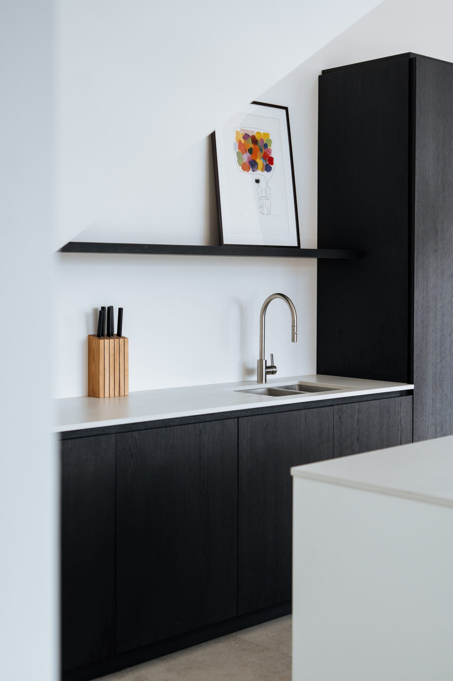 Moderne keuken met zwarte onderkasten, wit werkblad en zwarte wandplank in Knokke-Heist, Kaster Keukens
