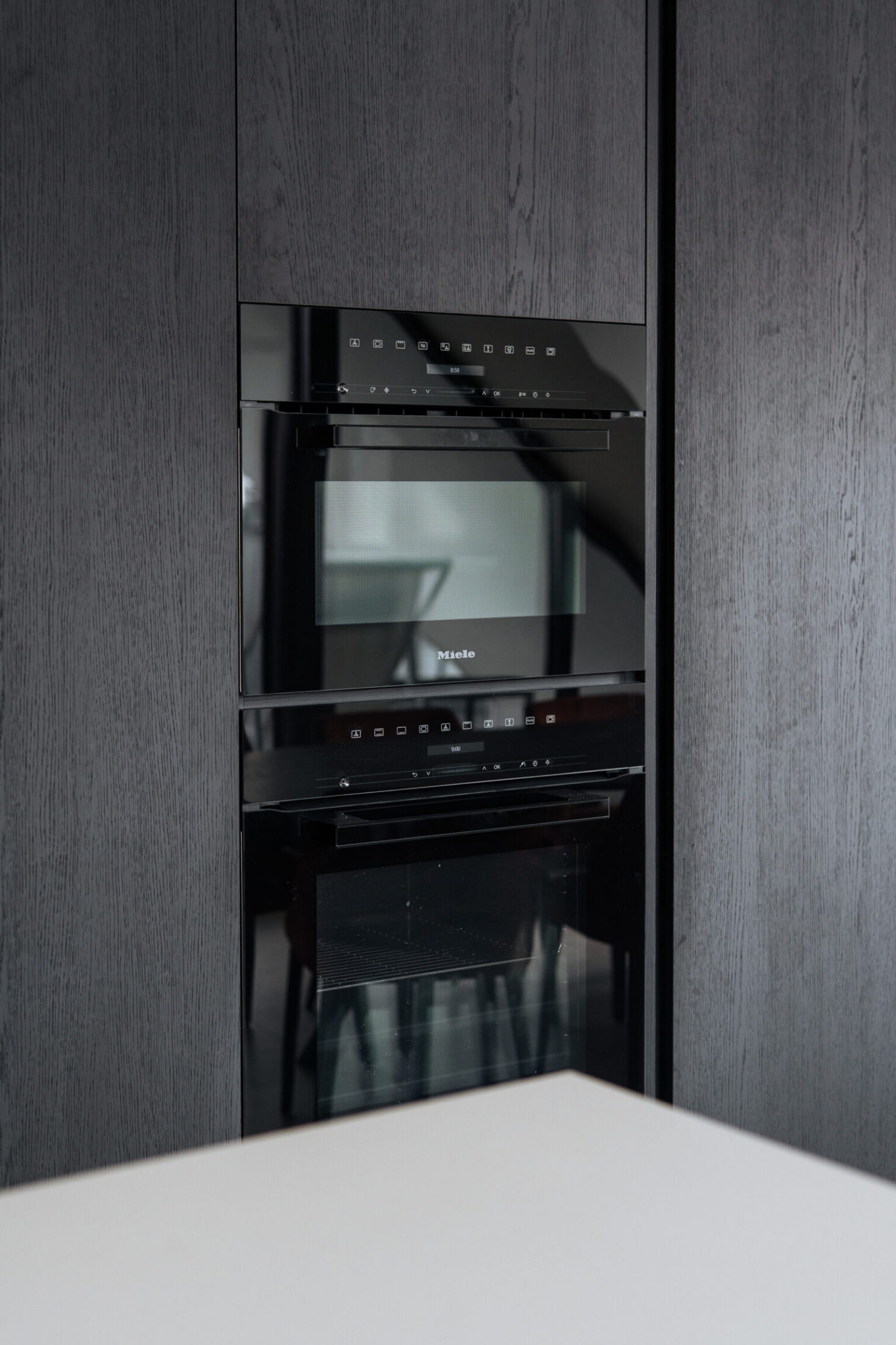 Detail van een moderne keuken met zwarte houten hoge kast en ingebouwde oven in Knokke-Heist, Kaster Keukens