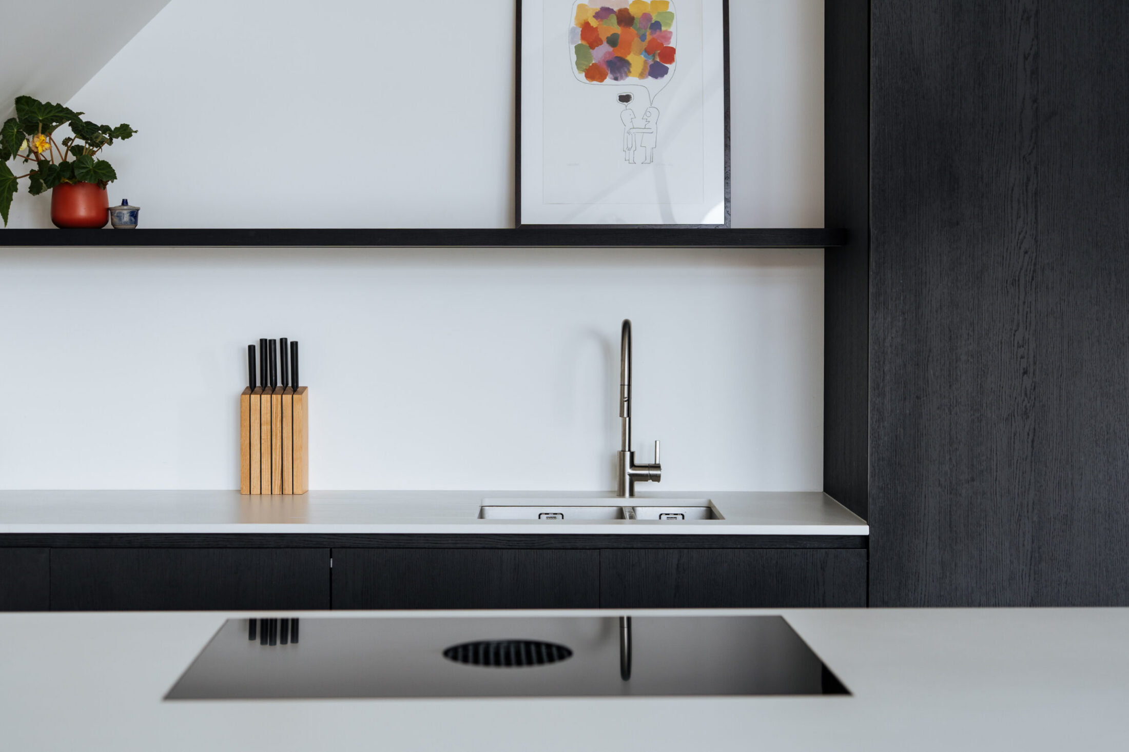 Detail van een moderne keuken met inox spoelbak, zwarte wandplank en kookplaat in het eiland in Knokke-Heist, Kaster Keukens