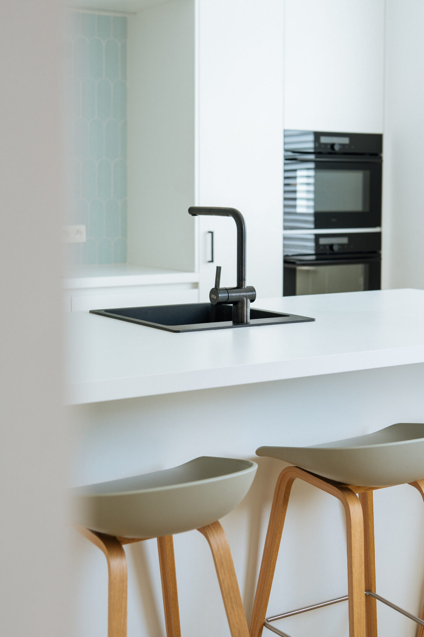 Detail van een moderne keuken met wit eiland, zwarte kraan en houten barkrukken in Moorslede, Kaster Keukens