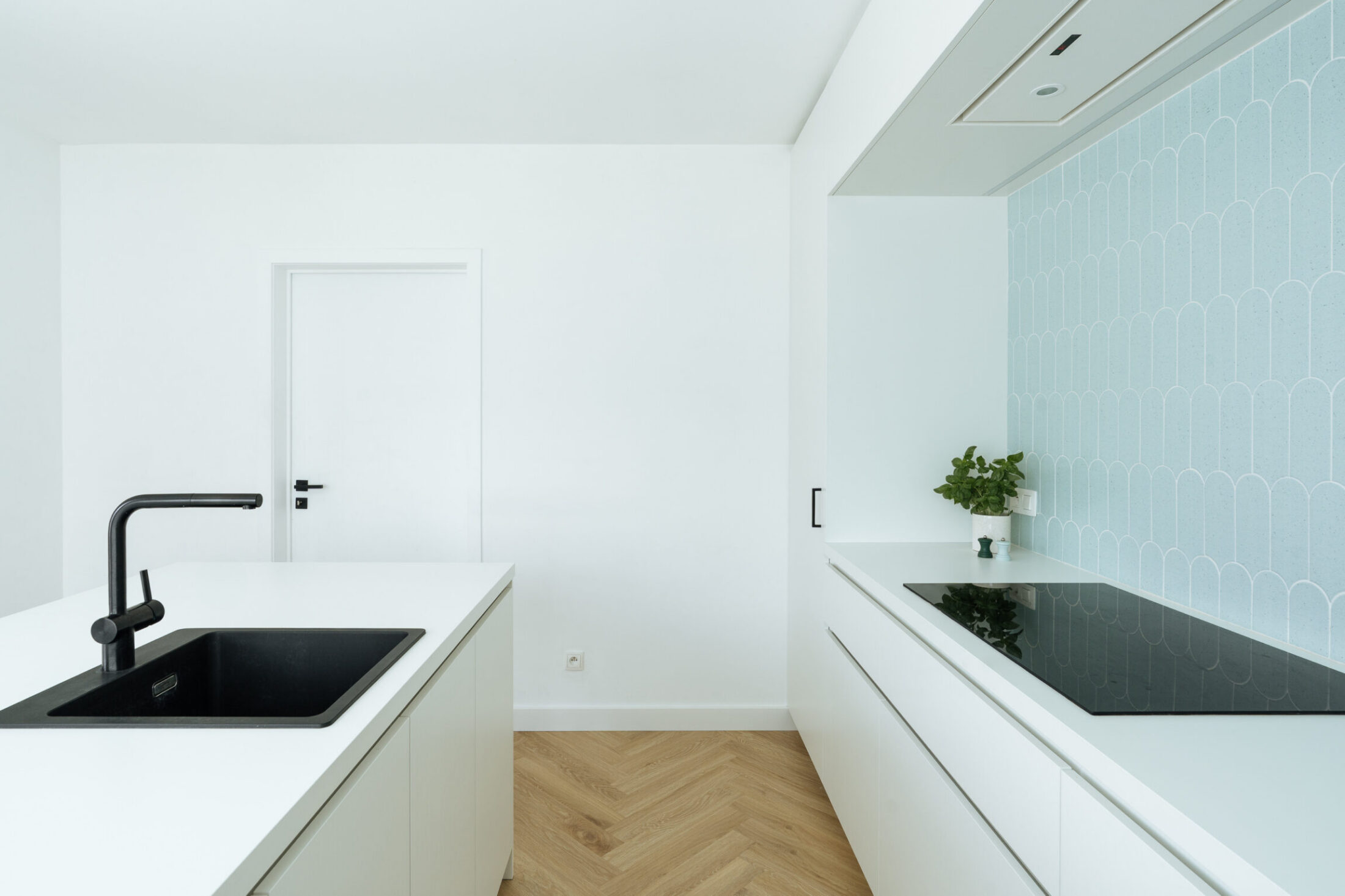 Moderne keuken met witte fronten, zwarte spoelbak, kookplaat en visgraatvloer in Moorslede, Kaster Keukens