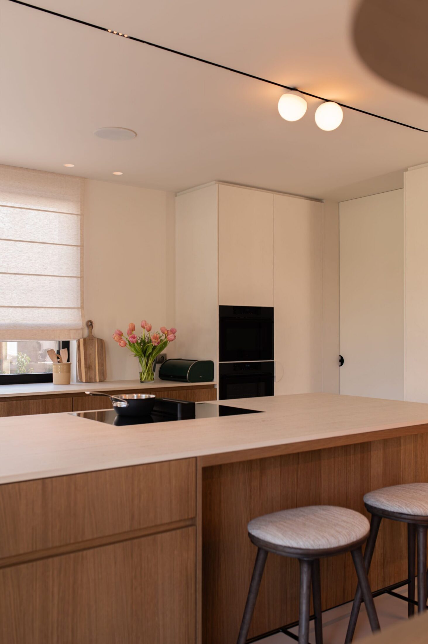 Detail van een Scandinavische keuken met eiken eiland, barkrukken en witte hoge kasten met ovens in Roeselare, Kaster Keukens