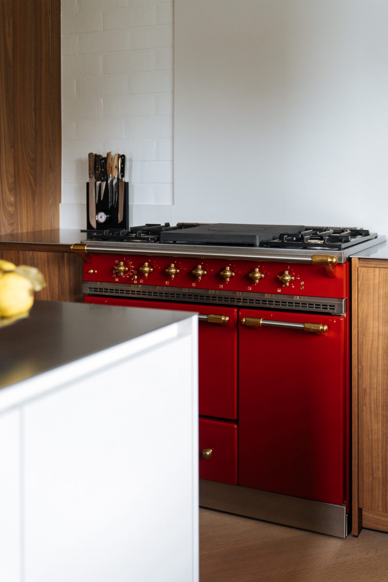 Detail van een moderne keuken met rood fornuis, wit eiland en notelaar fronten in Izegem, Kaster Keukens