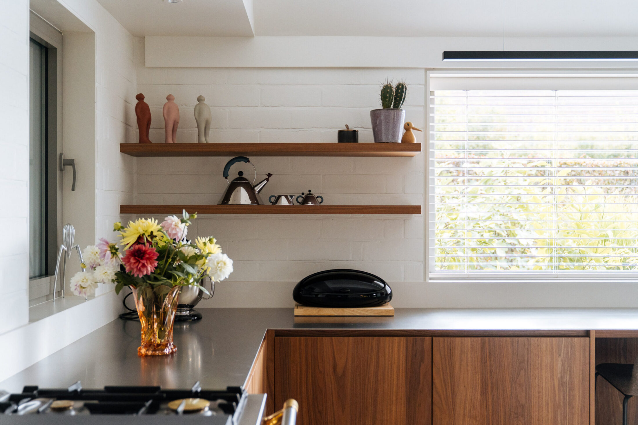 Moderne keuken met notelaar onderkasten, donker werkblad en houten wandplanken onder het raam in Izegem, Kaster Keukens