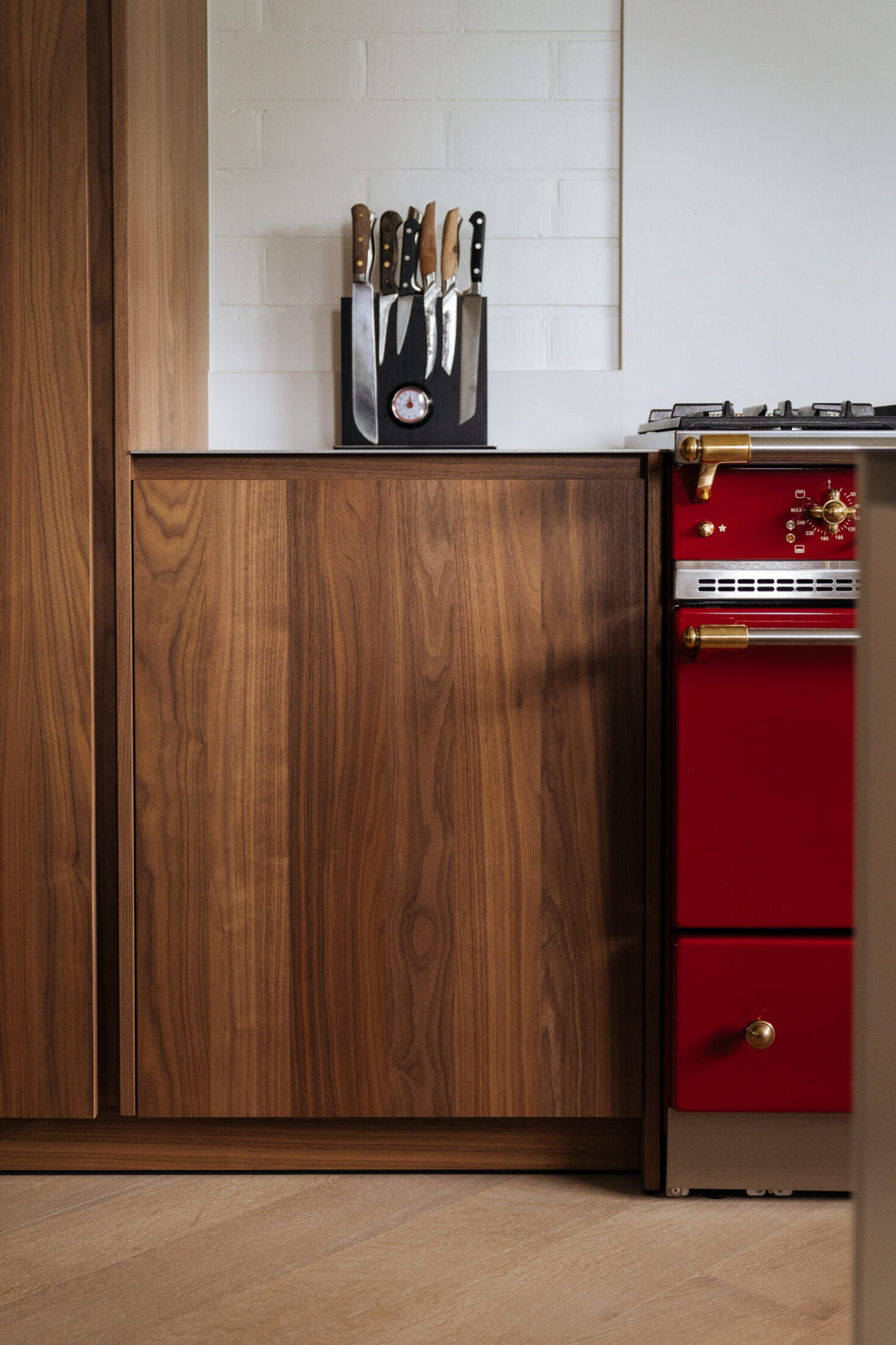 Detail van een moderne keuken met notelaar fronten naast een rood fornuis in Izegem, Kaster Keukens
