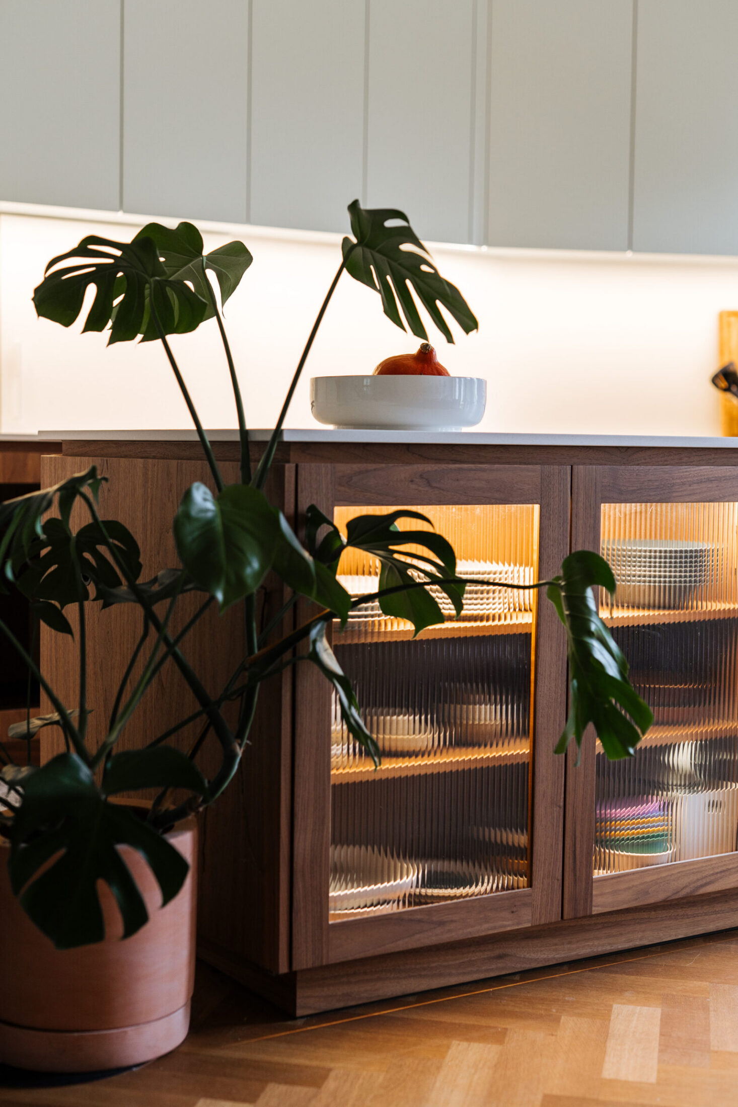 Detail van een moderne keuken met notelaar vitrinekasten met glazen deuren en verlichting in Kortrijk, Kaster Keukens