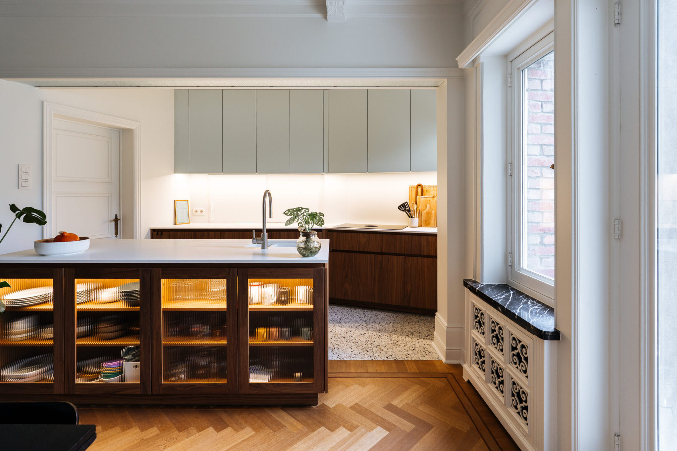 Moderne keuken met notelaar eiland met glazen vitrinedeuren en lichtgroene bovenkasten in Kortrijk, Kaster Keukens