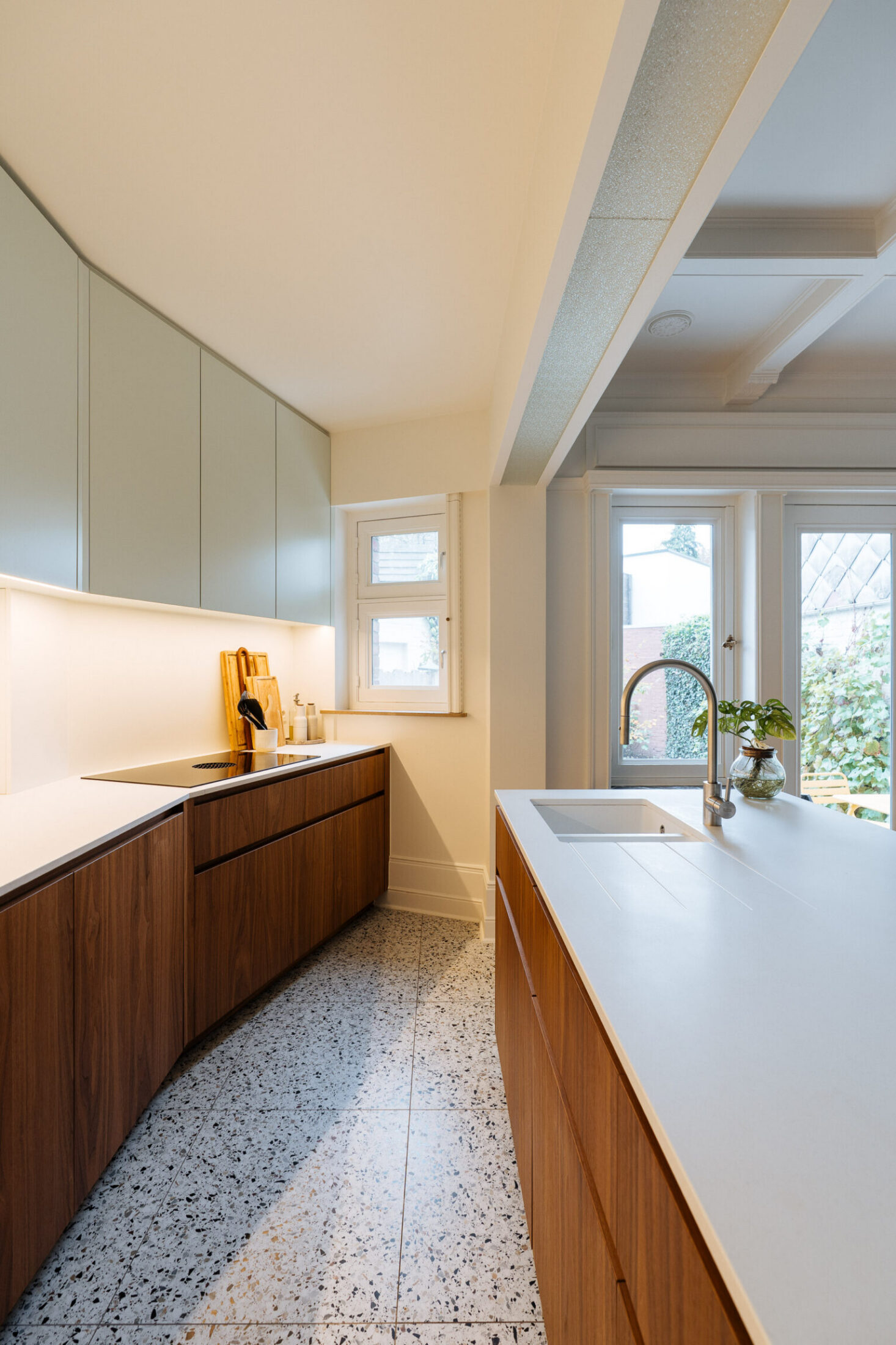Moderne keuken met notelaar onderkasten, wit werkblad en terrazzo vloer in Kortrijk, Kaster Keukens