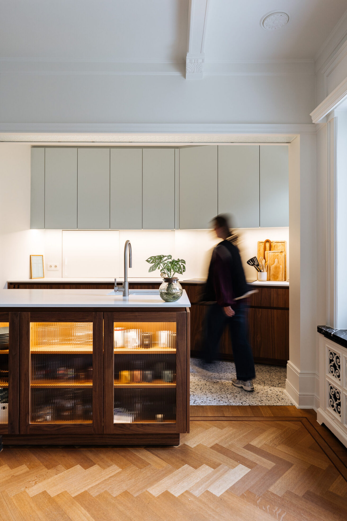 Moderne keuken met notelaar eiland, lichtgroene bovenkasten en visgraatvloer in Kortrijk, Kaster Keukens