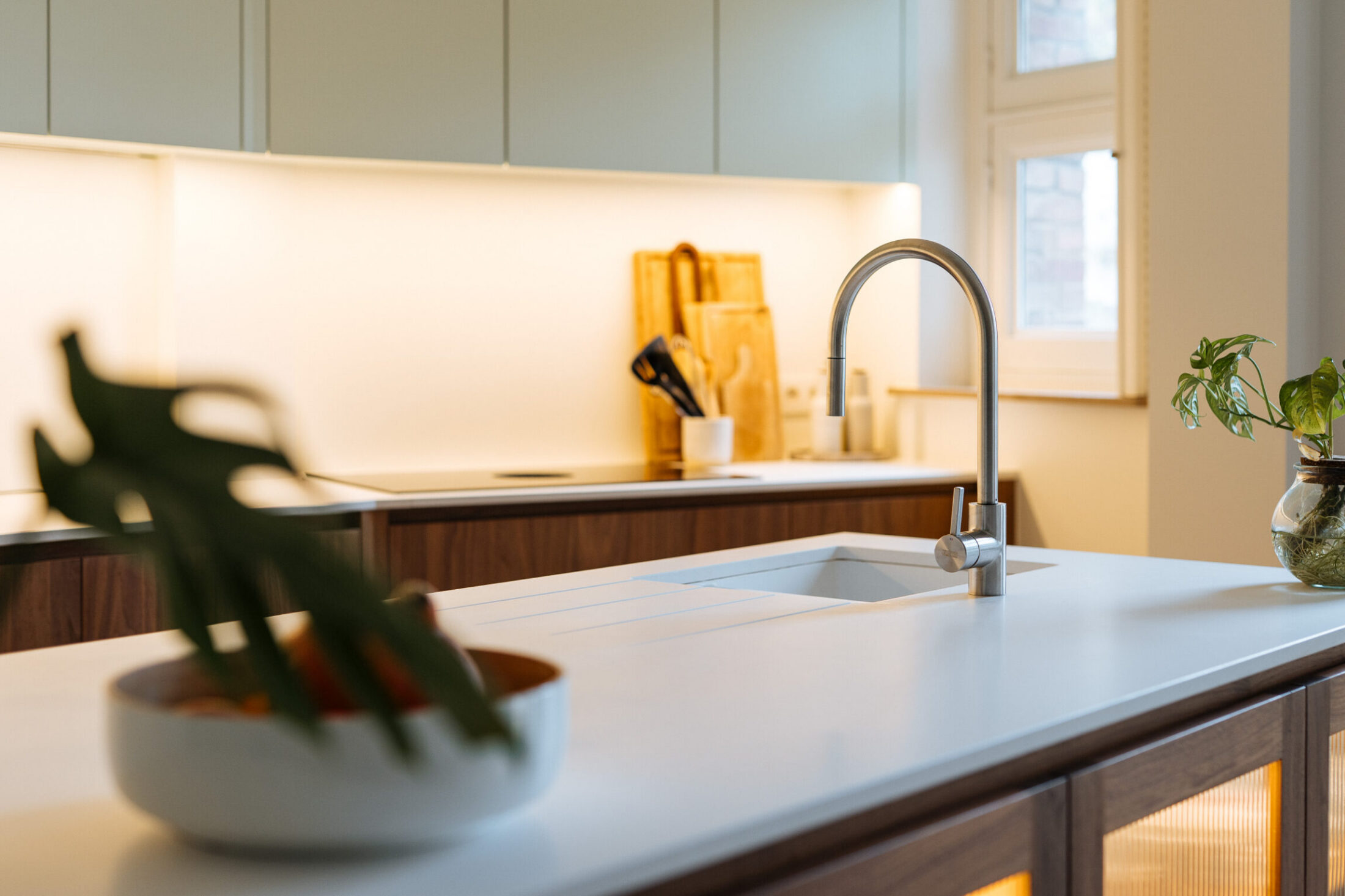 Detail van een moderne keuken met wit werkblad, inox kraan en verlichte achterwand in Kortrijk, Kaster Keukens