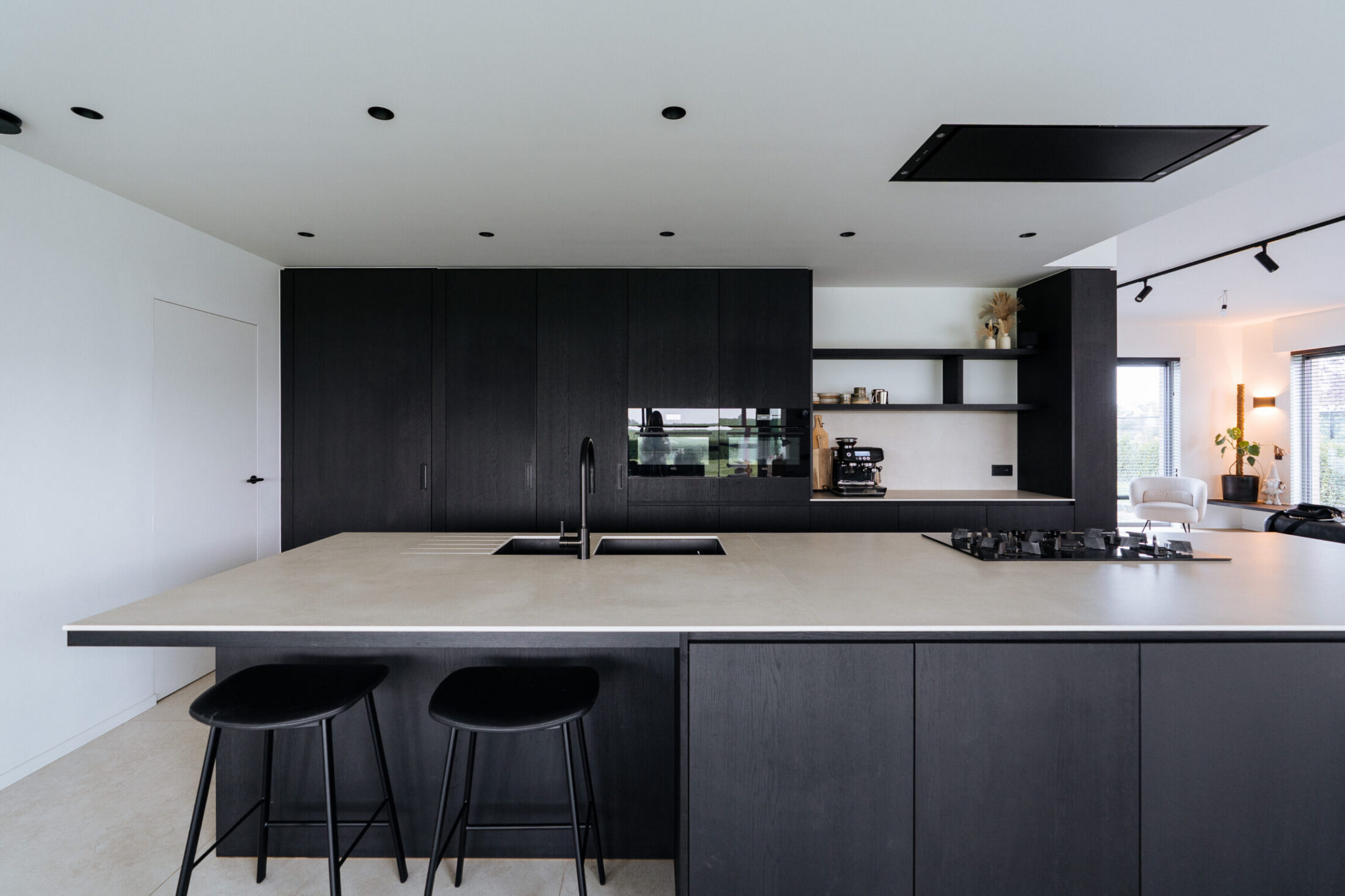 Moderne keuken met zwarte fronten, groot kookeiland met licht werkblad en zwarte barkrukken in Moorsele, Kaster Keukens