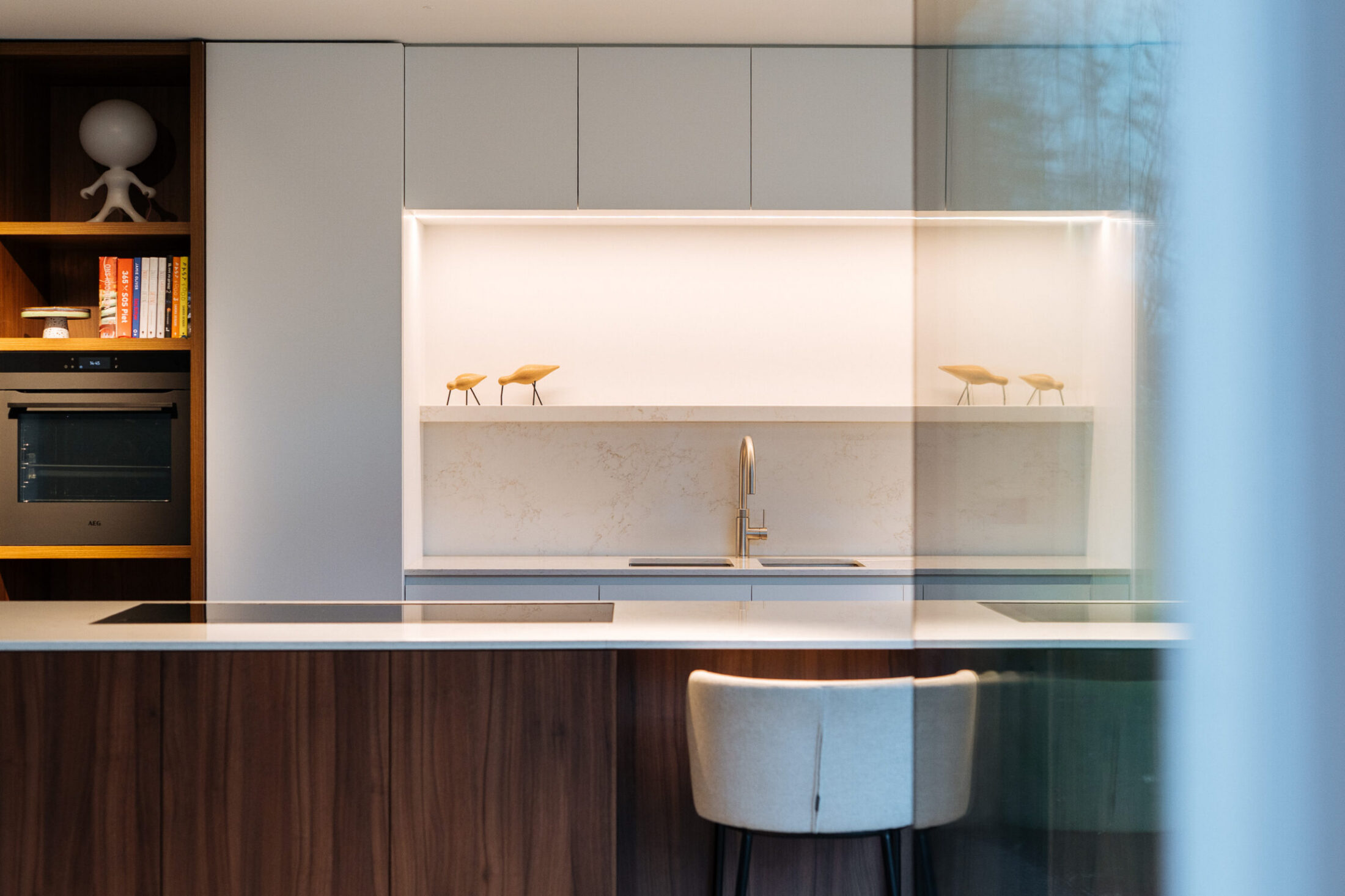 Moderne keuken met notelaar eiland, lichtgrijze kasten en verlichte nis met koperkleurige kraan in Drongen, Kaster Keukens