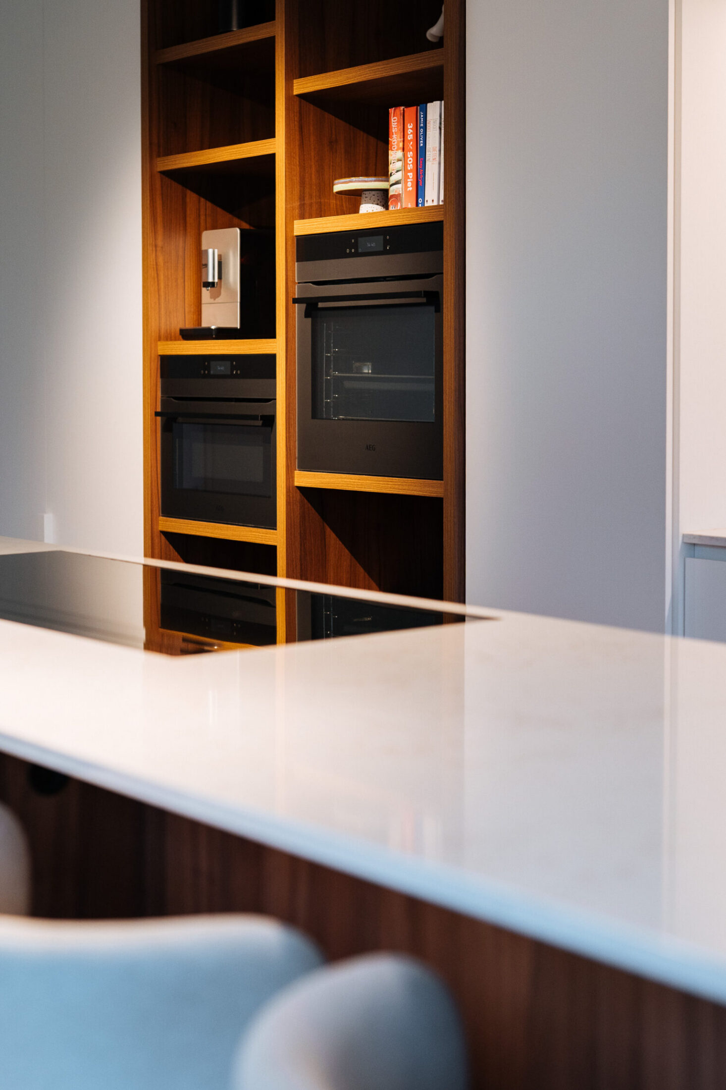 Detail van een moderne keuken met wit werkblad op het eiland en houten ovenkast op de achtergrond in Drongen, Kaster Keukens