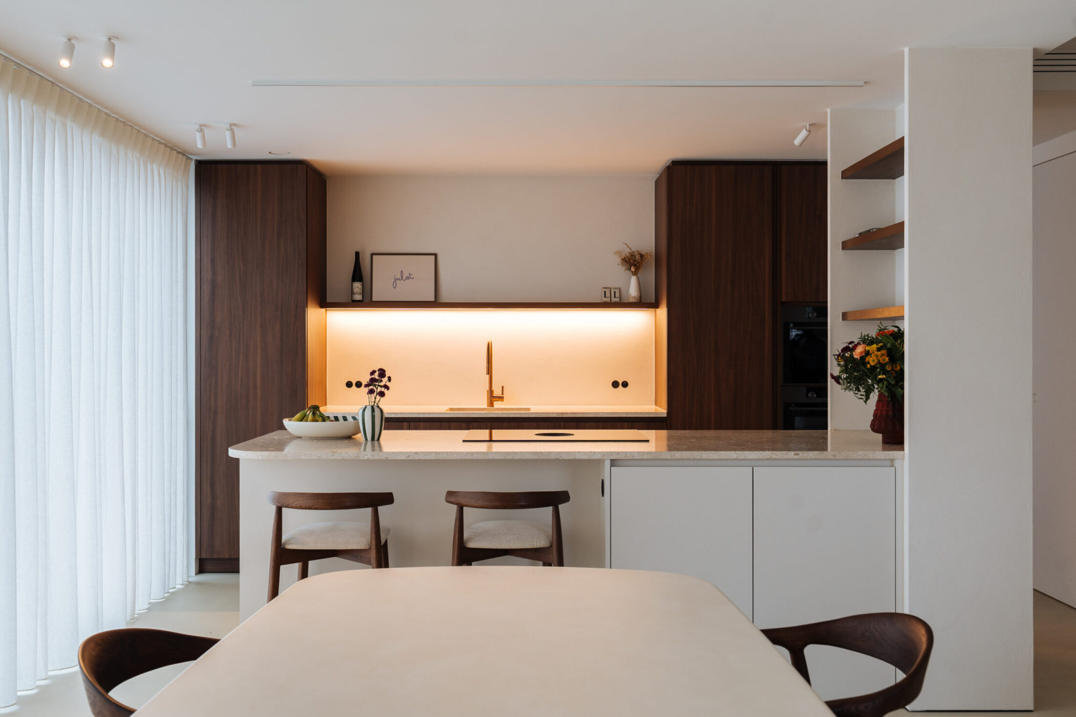 Moderne keuken met notelaar kasten, wit eiland met barkrukken en verlichte nis in Zwevegem, Kaster Keukens