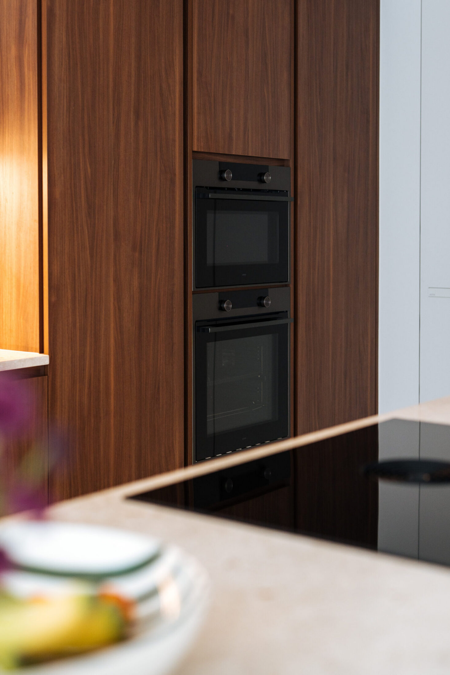 Detail van een moderne keuken met notelaar kastenwand, ingebouwde ovens en kookplaat in Zwevegem, Kaster Keukens