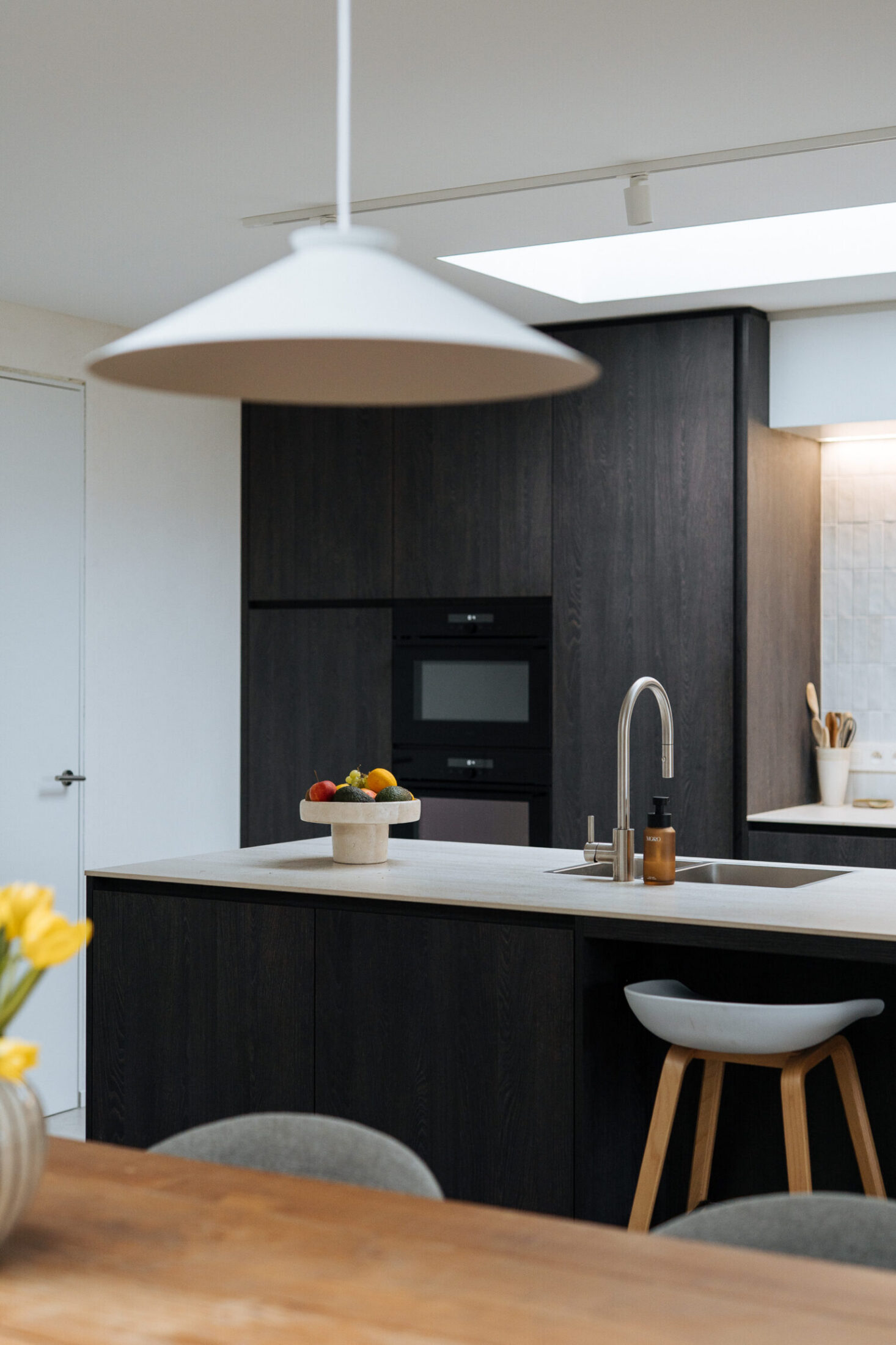 Moderne keuken met donkere fronten, kookeiland met wit werkblad en witte hanglamp in Ardooie, Kaster Keukens