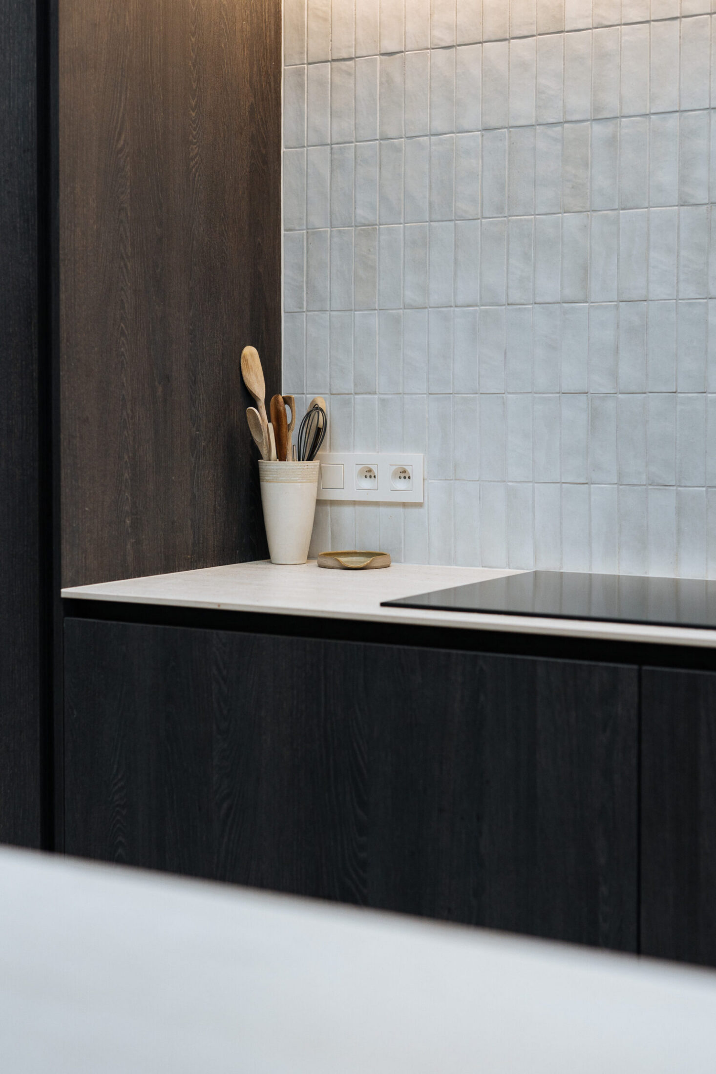 Detail van een moderne keuken met donkere fronten, wit werkblad en lichtgrijze wandtegels in Ardooie, Kaster Keukens