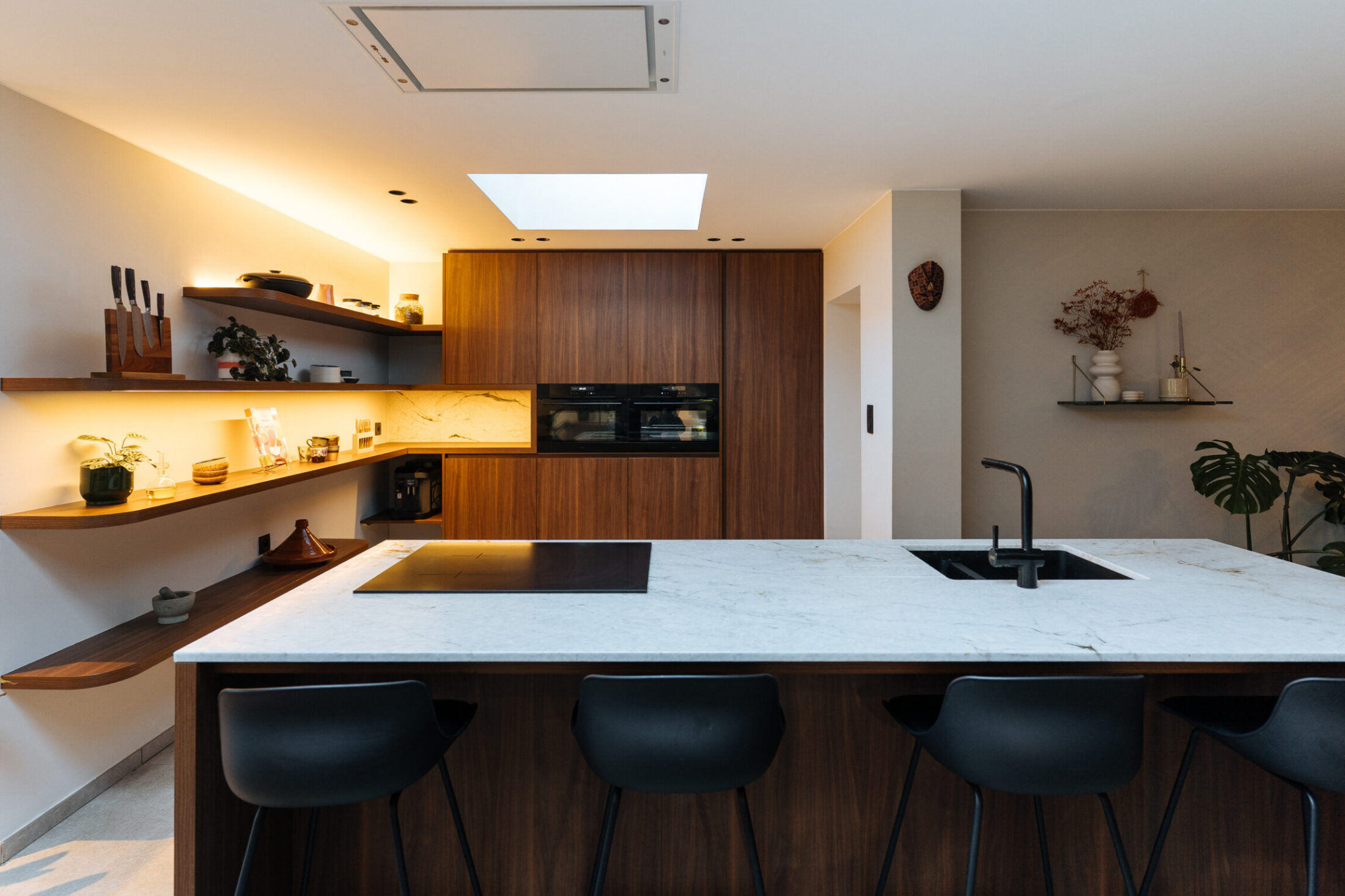 Moderne keuken met marmerlook kookeiland, zwarte barkrukken en notelaar kastenwand in Hooglede, Kaster Keukens