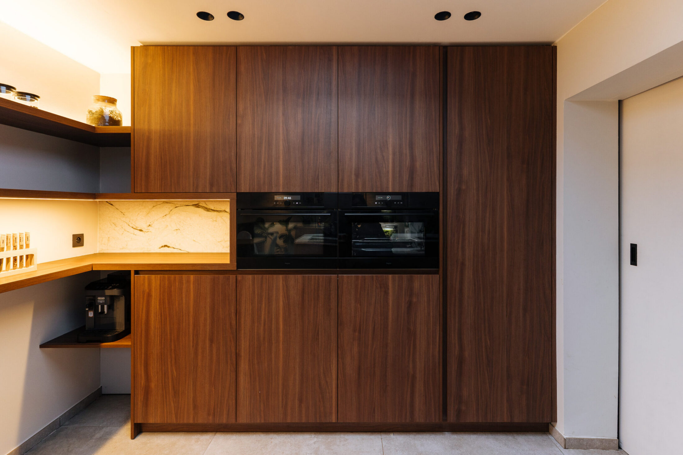 Moderne keuken met notelaar kastenwand, twee inbouwovens en verlichte hoekrekken in Hooglede, Kaster Keukens