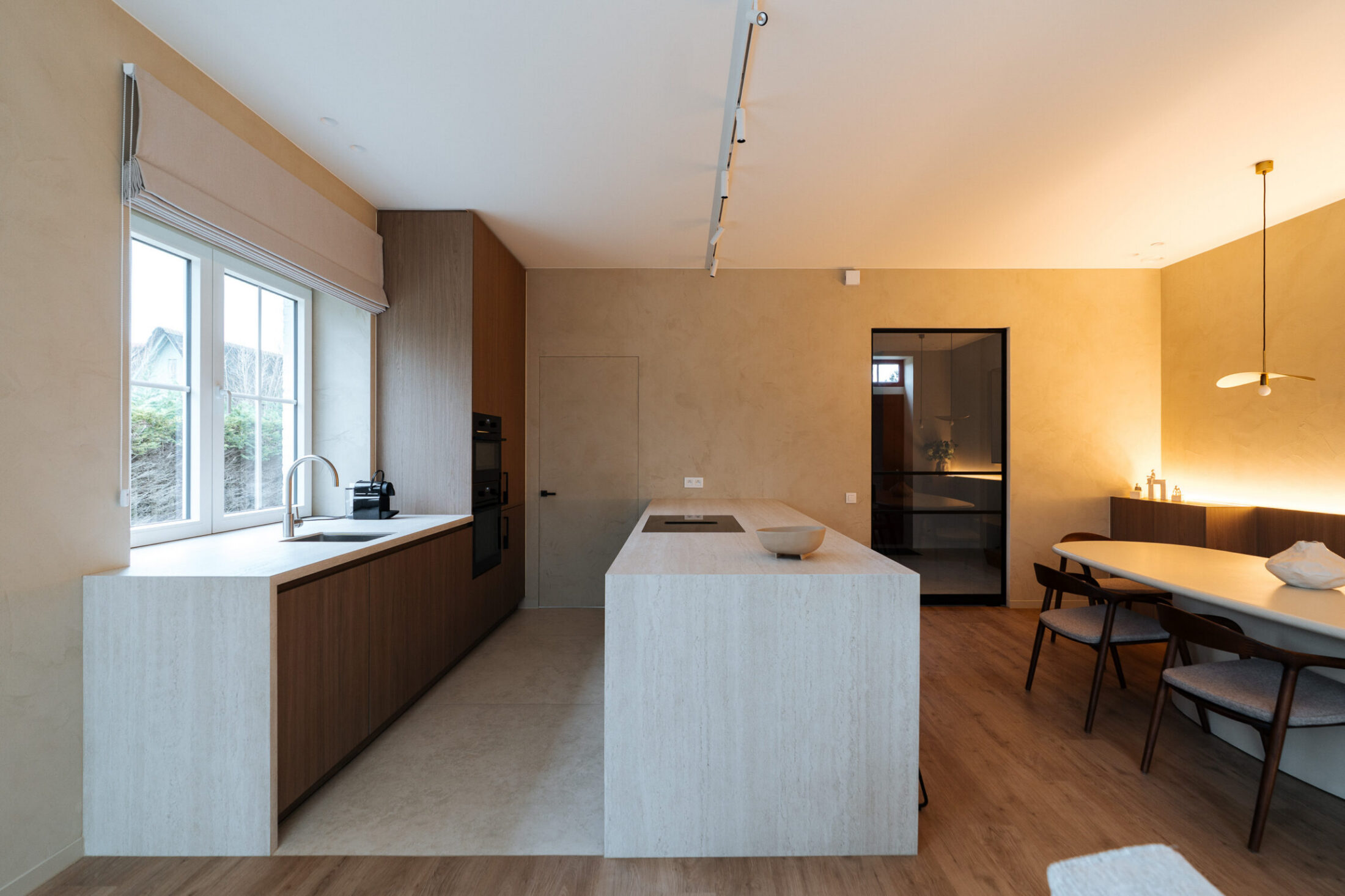 Moderne keuken met licht natuurstenen eiland, notelaar kasten en open eetruimte in Oostduinkerke, Kaster Keukens