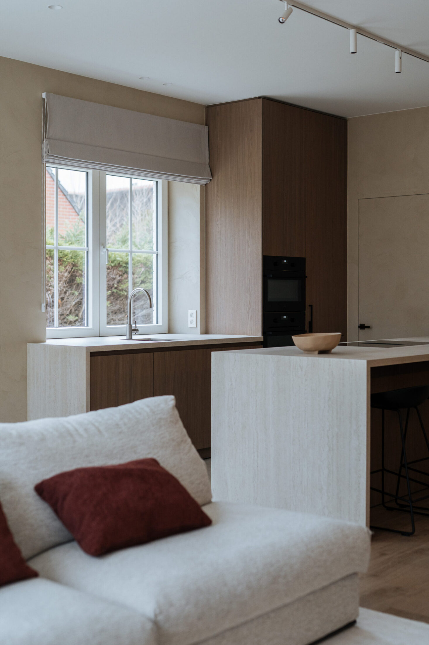 Moderne keuken met lichte stenen fronten en notelaar hoge kast, gezien vanuit de zithoek in Oostduinkerke, Kaster Keukens
