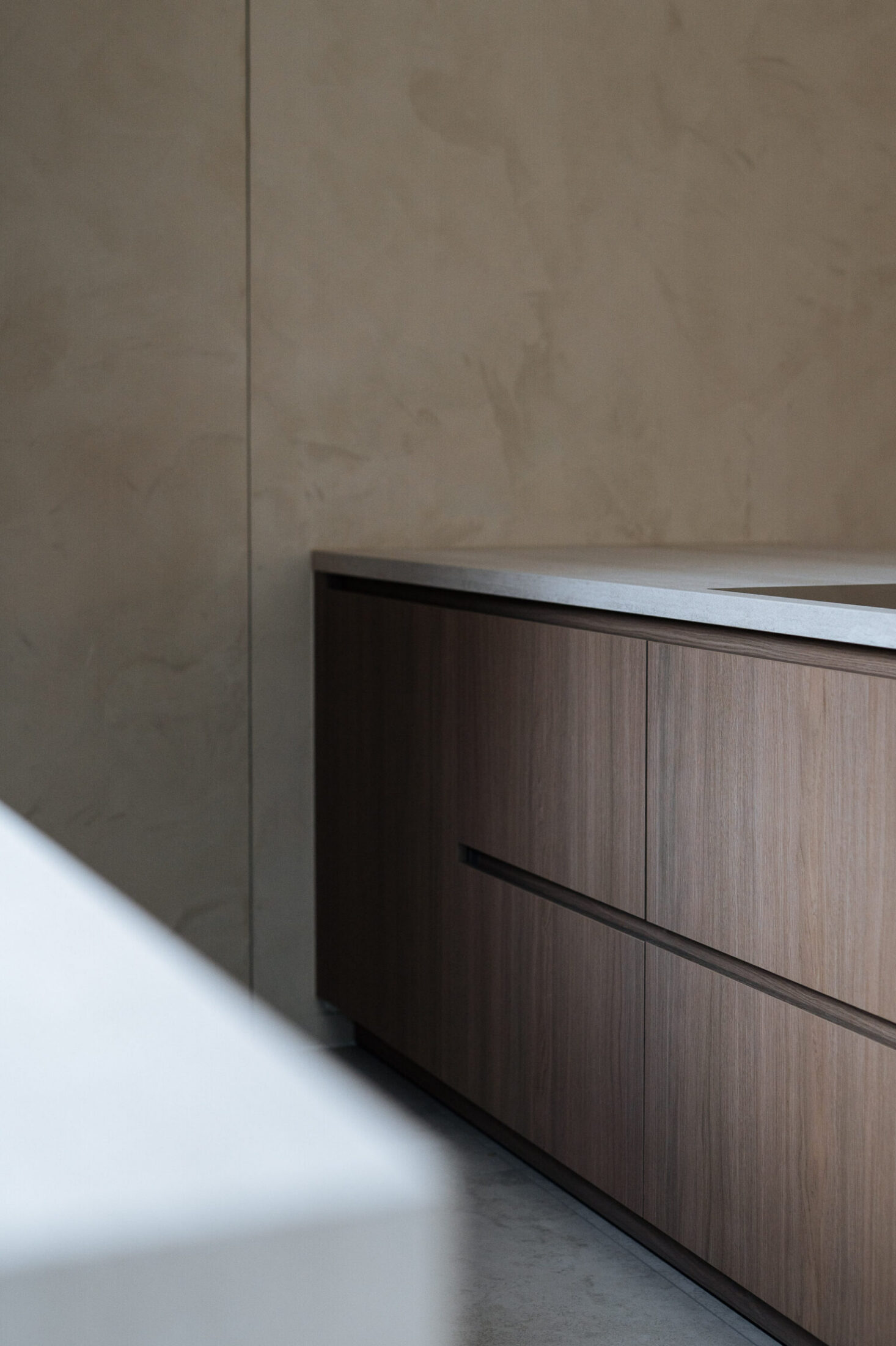 Detail van een moderne keuken met grepenloze notelaar laden en licht werkblad in Oostduinkerke, Kaster Keukens