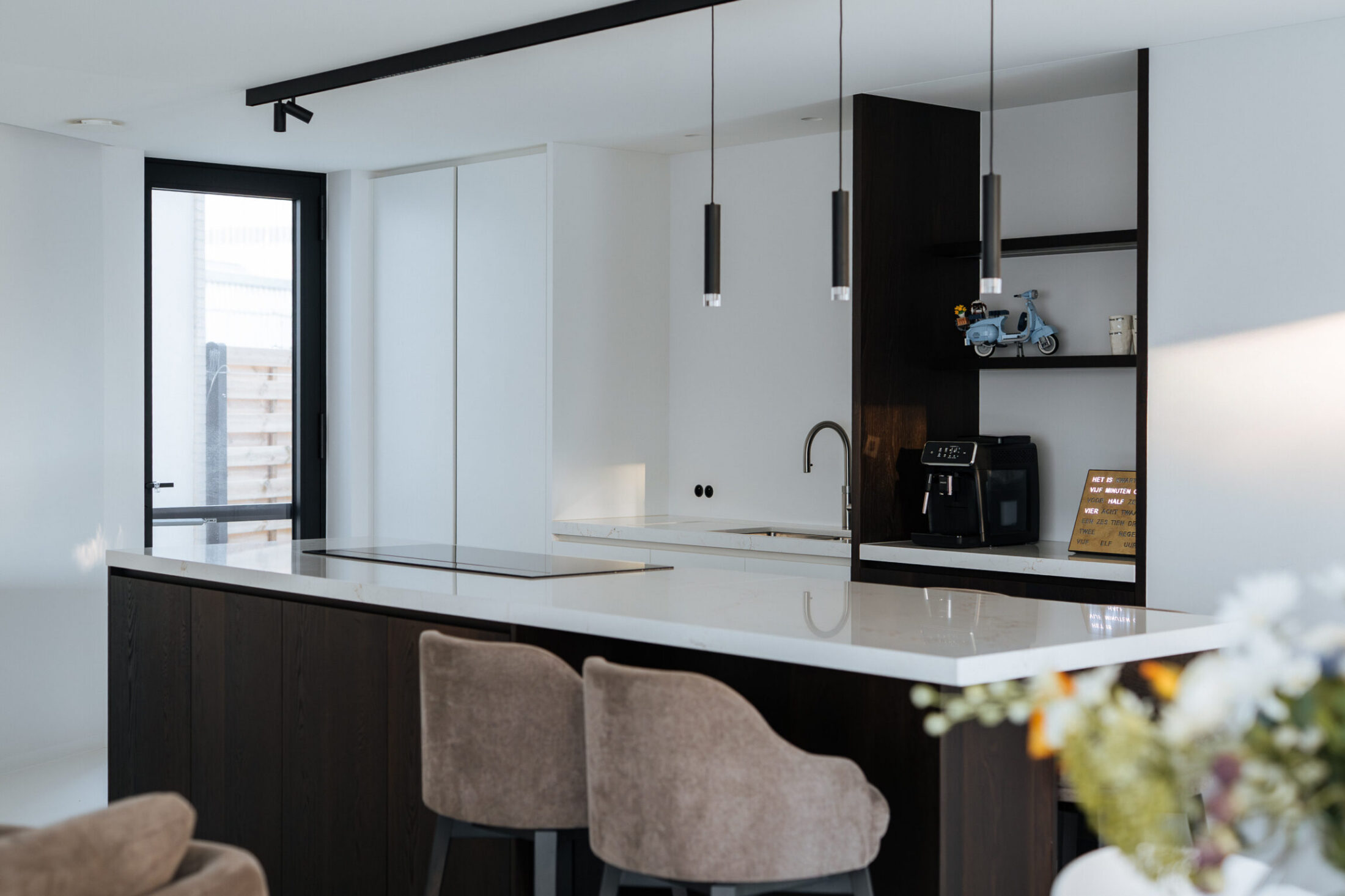 Moderne keuken met donker houten kookeiland, wit werkblad en beige barkrukken in Oostnieuwkerke, Kaster Keukens