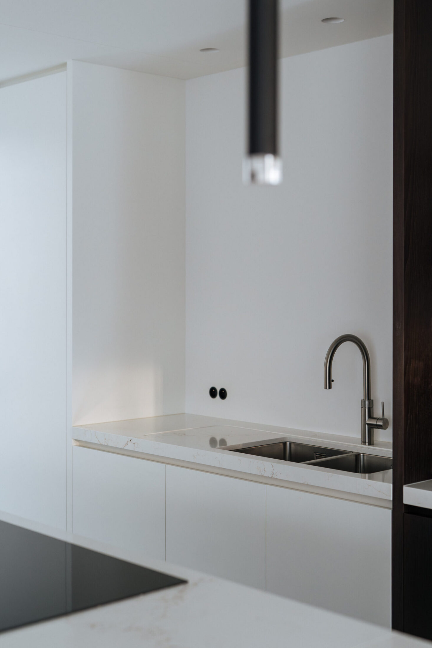 Detail van een moderne keuken met witte kasten, inox spoelbak en zwarte hanglamp in Oostnieuwkerke, Kaster Keukens