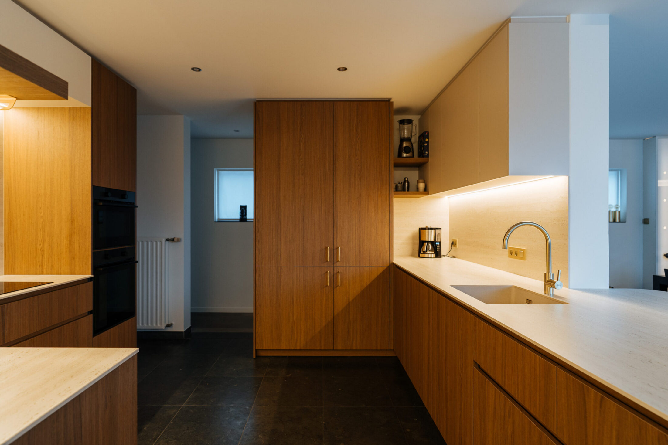 Moderne keuken met houten fronten, wit werkblad en hoge kastenwand in Roeselare, Kaster Keukens