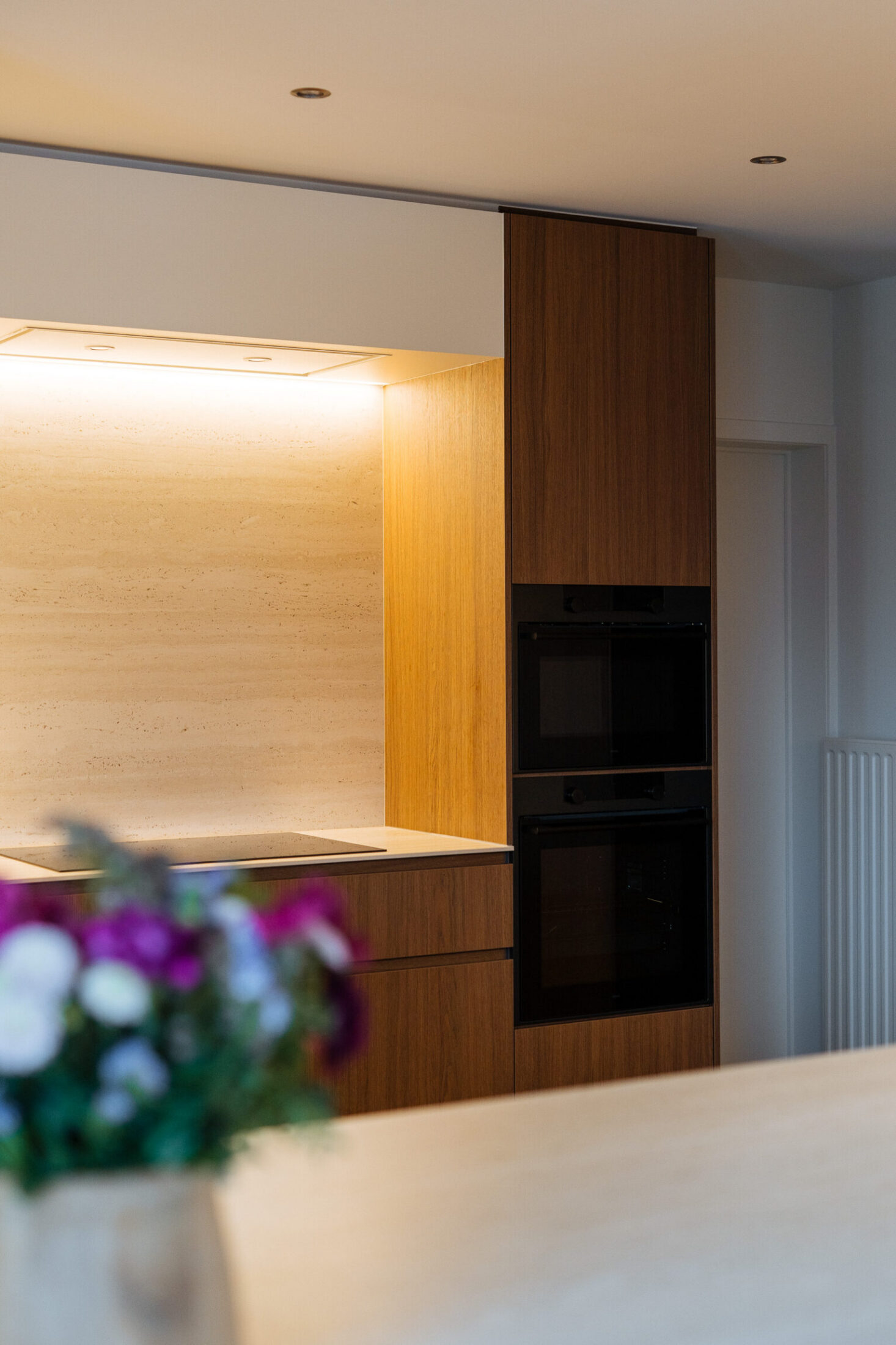 Detail van een moderne keuken met hoge houten kasten, ingebouwde ovens en ledverlichting in Roeselare, Kaster Keukens