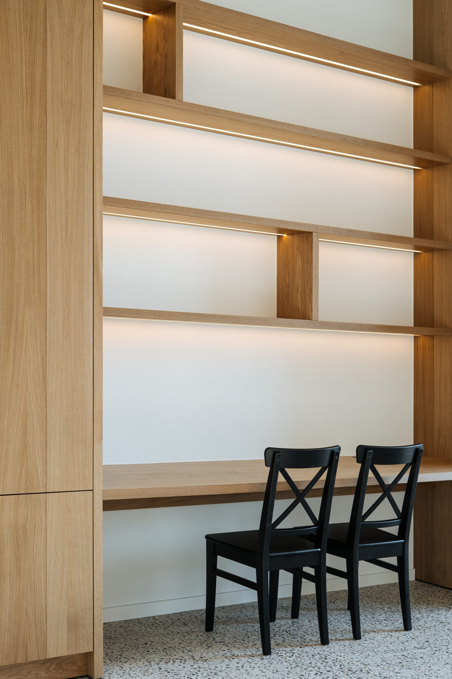 Detail van een bureau op maat met eiken rekken, verlichting en zwarte stoelen in Kortrijk, Kaster Keukens