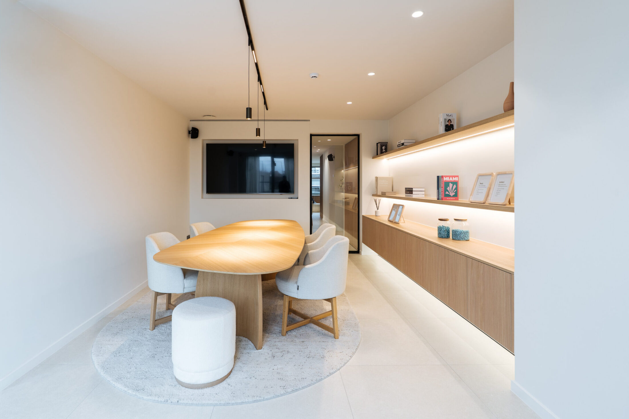 Vergaderzaal op maat met ovale houten tafel, verlichte wandrekken en ingebouwd scherm in Sijsele, Kaster Keukens