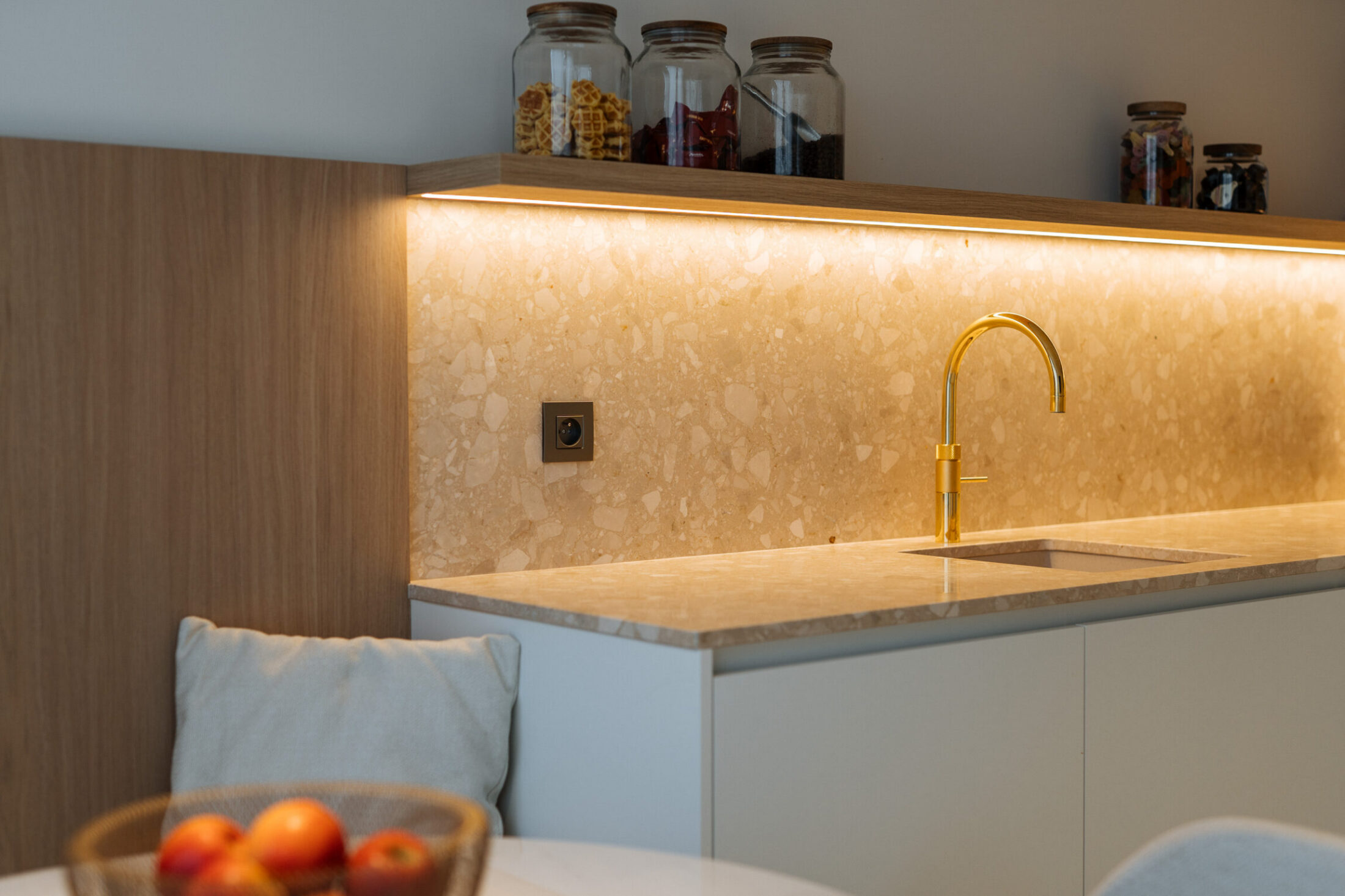 Detail van een kitchenette op maat met terrazzo spatwand, goudkleurige kraan en houten rek in Sijsele, Kaster Keukens
