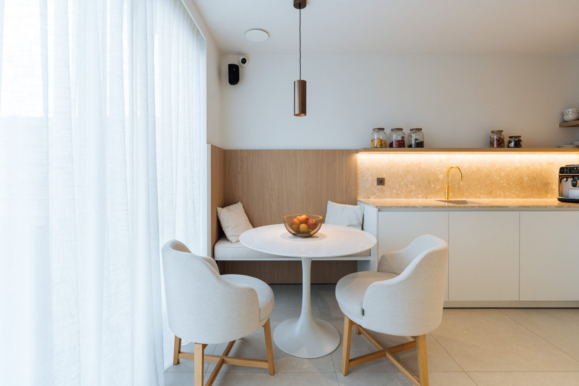 Kitchenette op maat met witte fronten, verlichte nis en ronde tafel in een zithoek in Sijsele, Kaster Keukens