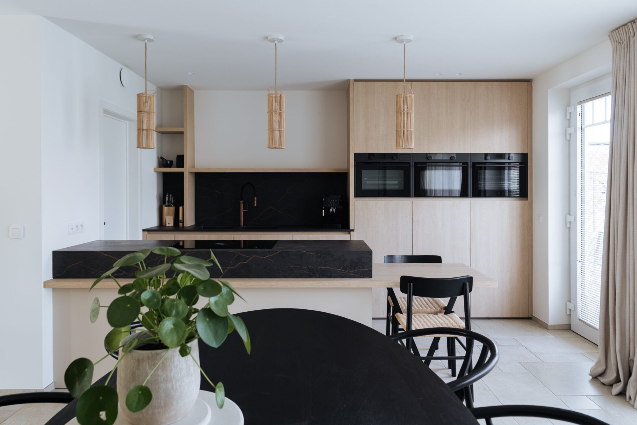 Moderne keuken met lichte houten kastenwand, zwart eiland en rieten hanglampen in Knokke-Heist, Kaster Keukens