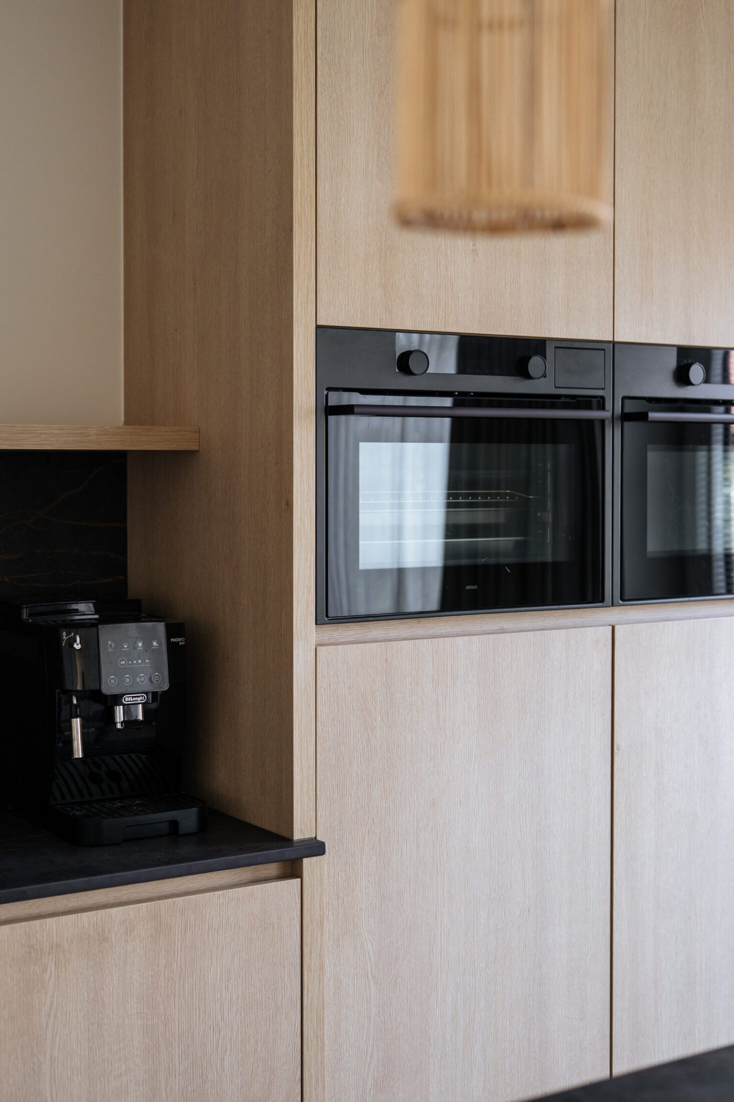 Detail van een moderne keuken met lichte houten hoge kasten en zwarte inbouwovens in Knokke-Heist, Kaster Keukens